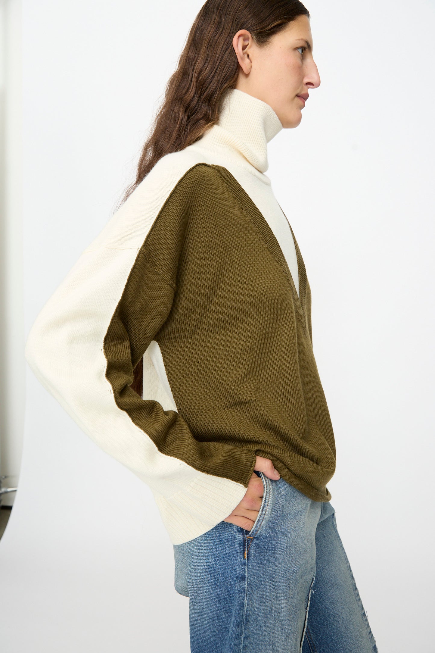 A person wears the MM6 Pullover in Off White-khaki, styled over blue jeans, and stands in profile against a plain background.