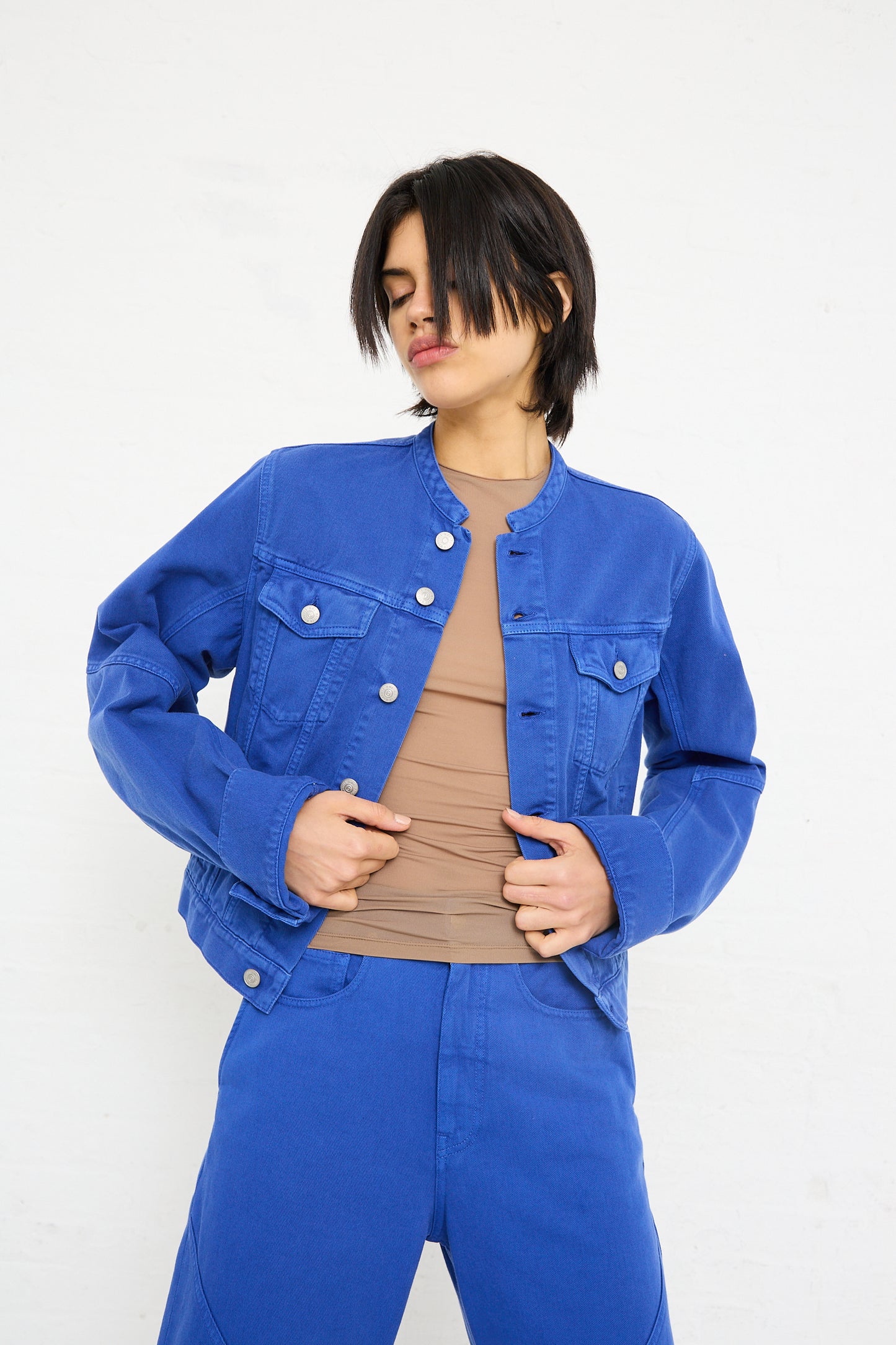 A woman in a blue MM6 Sports Jacket denim jacket and matching pants, standing against a white background, holding her jacket open.