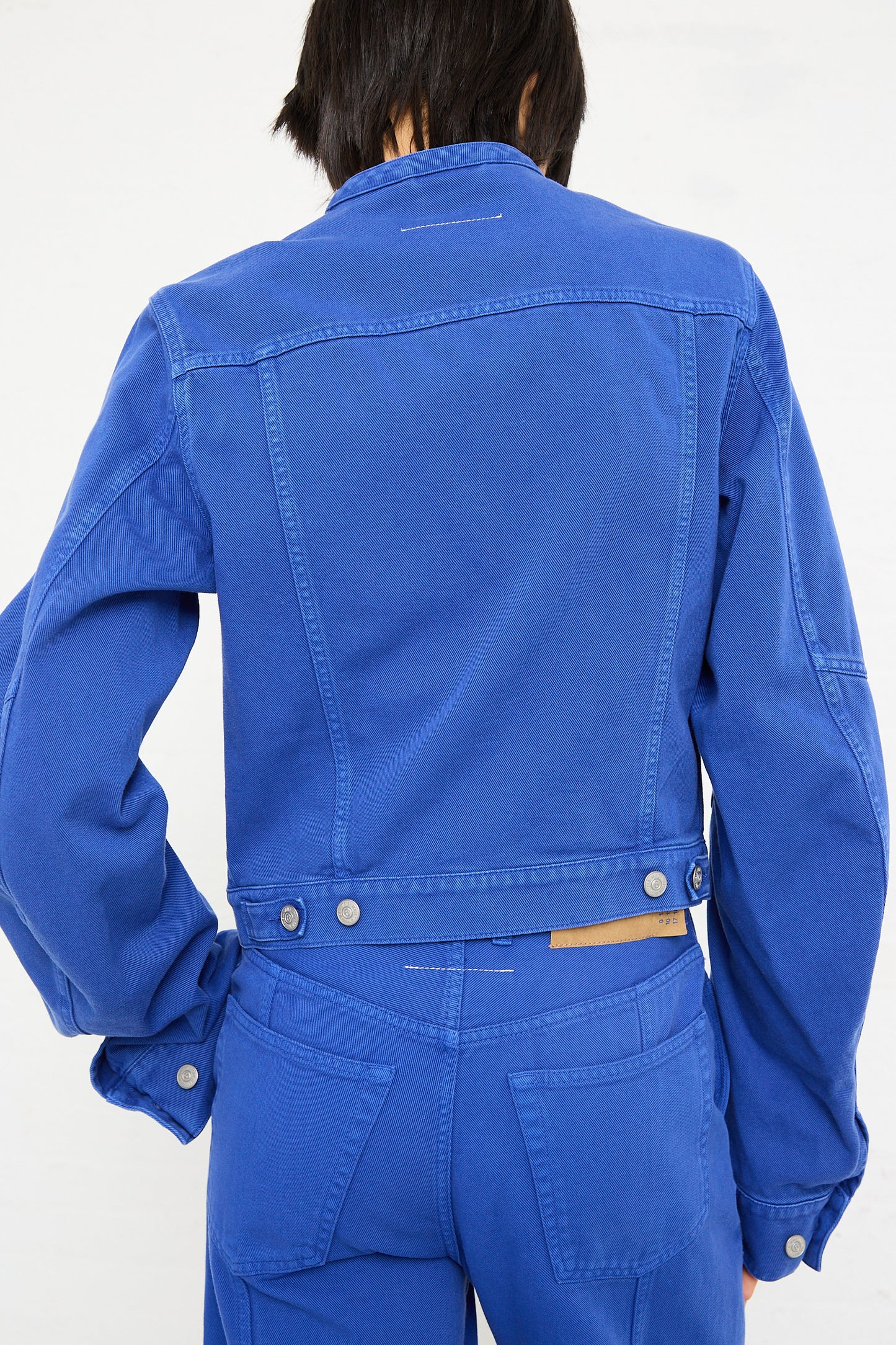 Rear view of a person wearing a bright blue MM6 Sports Jacket and matching jeans, standing against a white background.