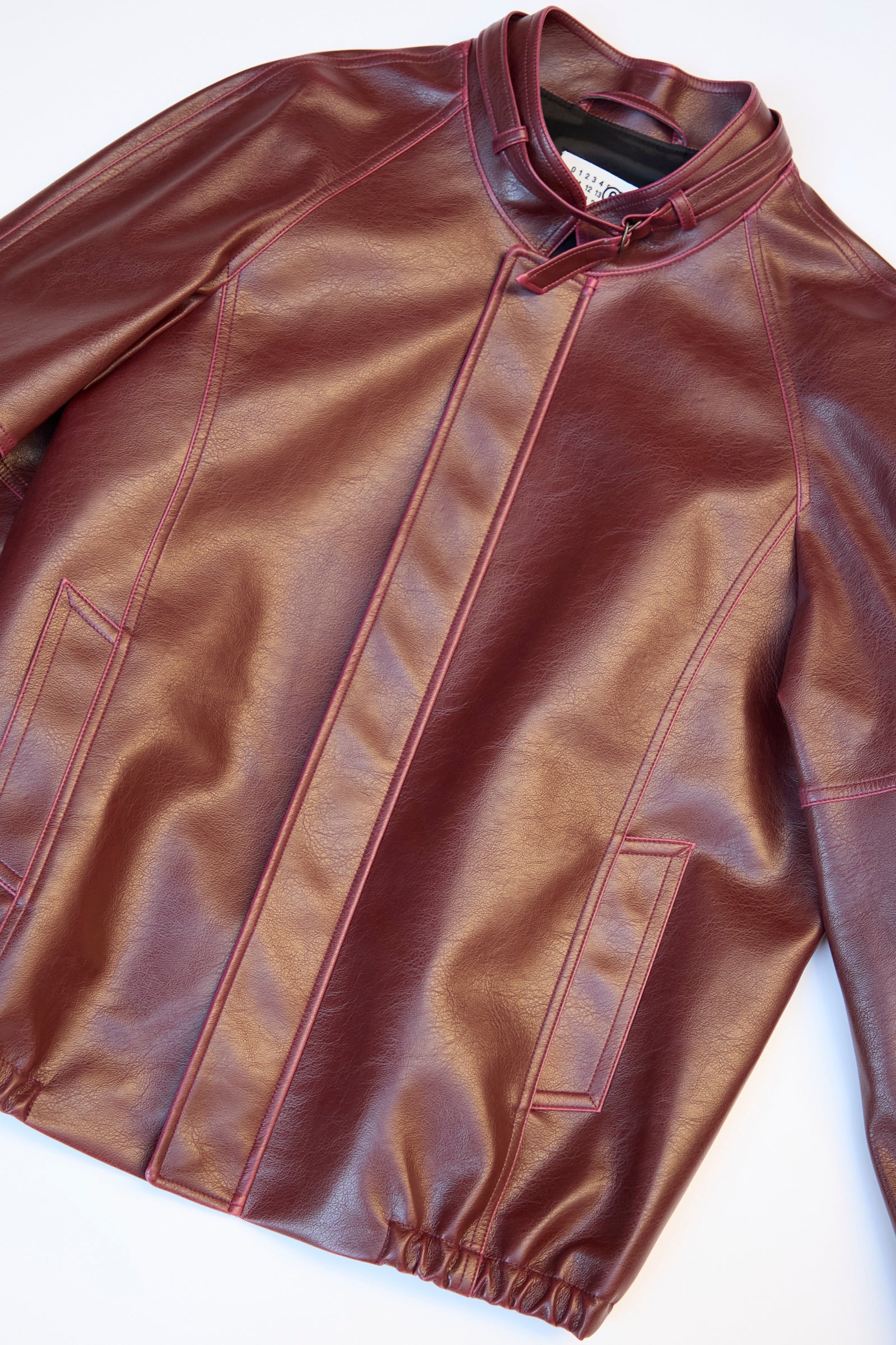 The MM6 Sports Jacket is a relaxed fit, faux-leather burgundy piece featuring a high collar, zipper hidden by a flap, and two side pockets.