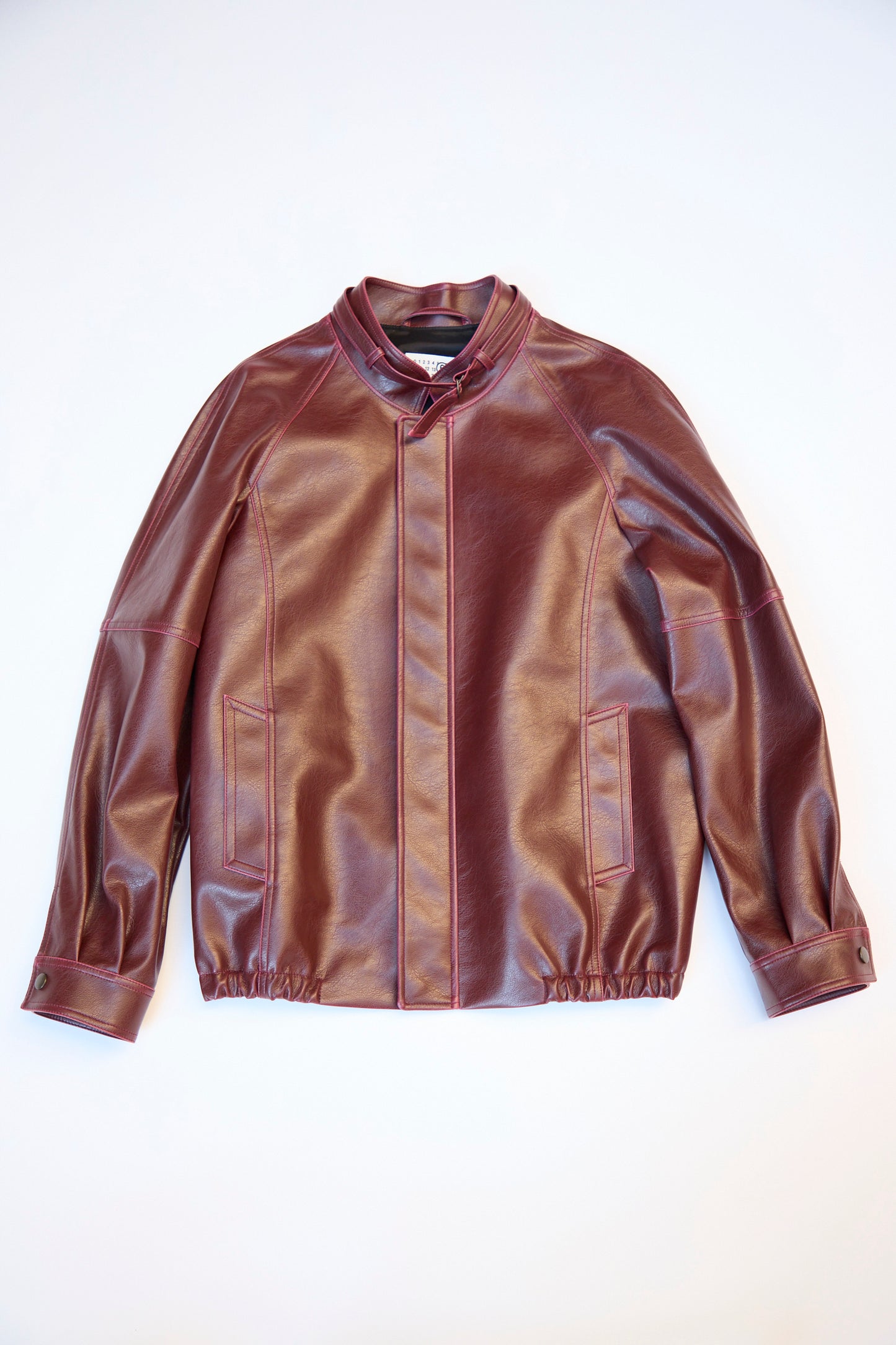 A burgundy MM6 Sports Jacket with a relaxed fit, stand-up collar, front snap buttons, and two pockets is laid flat on a white background.