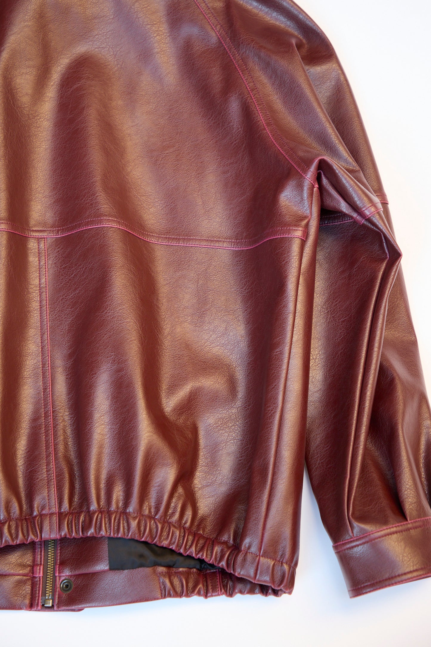 Close-up of an MM6 Sports Jacket in relaxed fit brown faux-leather, showcasing visible stitching and an elastic waistband, laid on a white surface.