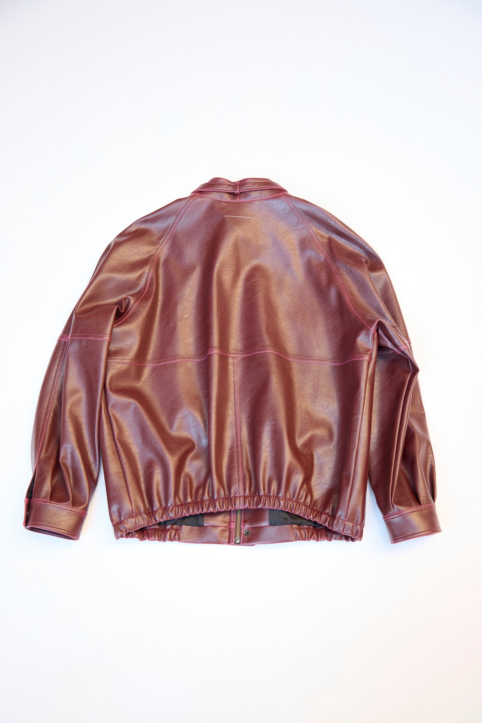 The MM6 Sports Jacket is a brown faux-leather piece with long sleeves, an elastic waistband, and visible seams. Laid flat on a light surface, it boasts a relaxed fit that combines style and comfort.