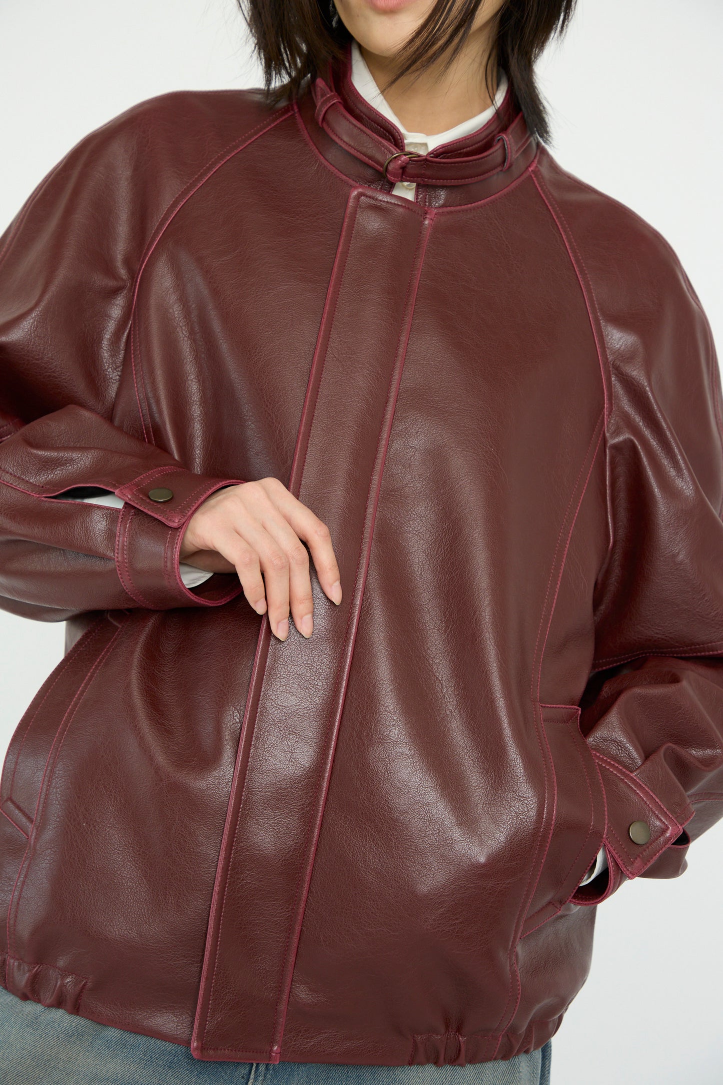 The individual is seen in an MM6 Sports Jacket, crafted from burgundy faux leather, hands casually resting on the front.