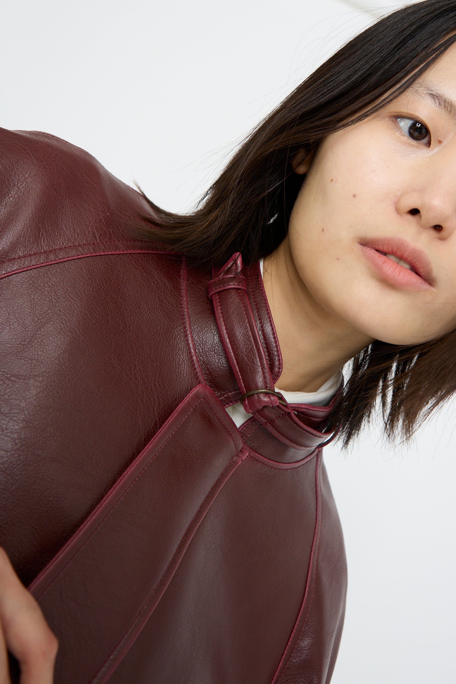 A person dressed in an MM6 Sports Jacket in burgundy faux-leather confidently looks at the camera against a plain white backdrop.