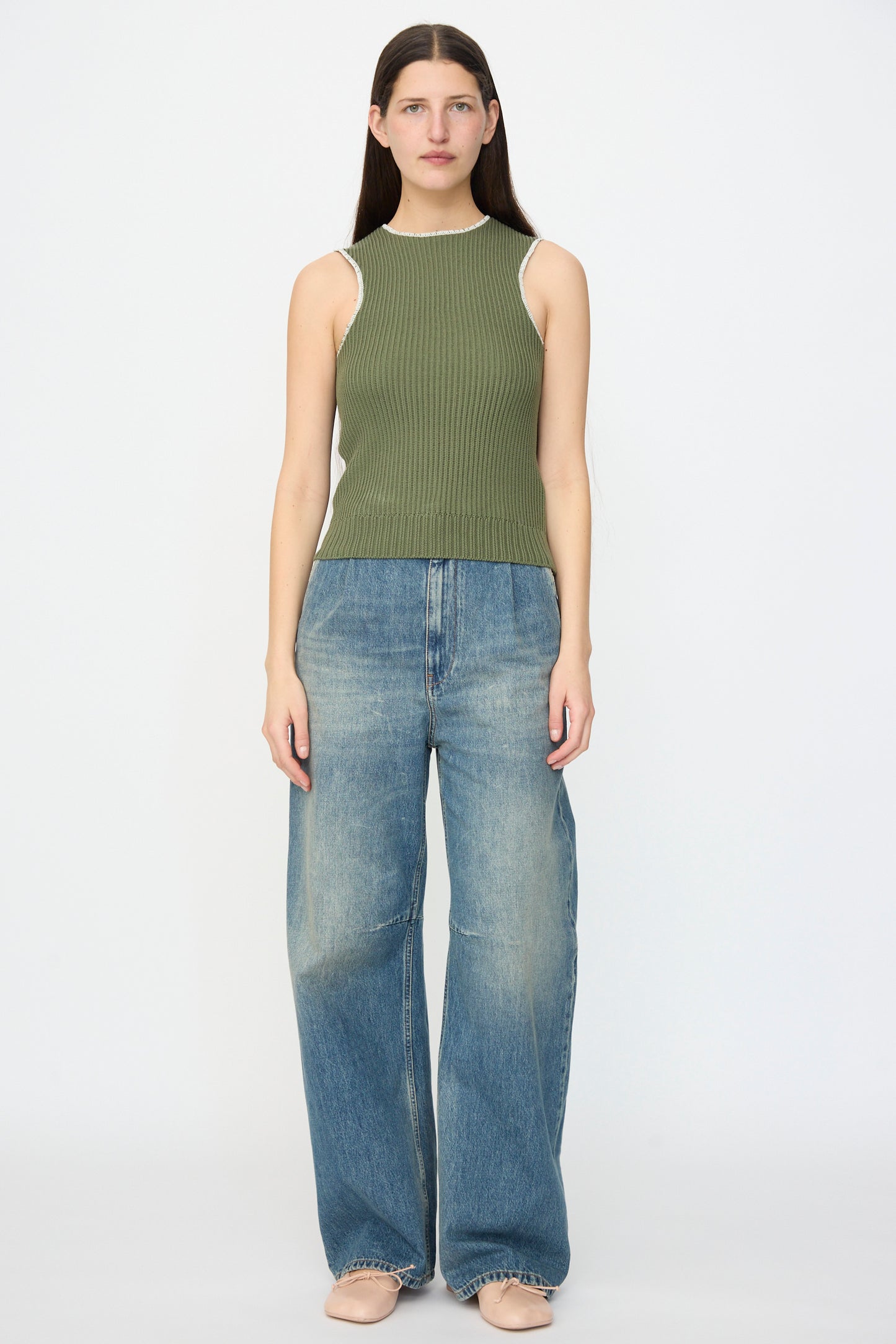 A person faces forward in an MM6 Top in Khaki, styled with wide-leg blue jeans and beige shoes, against a plain white background.