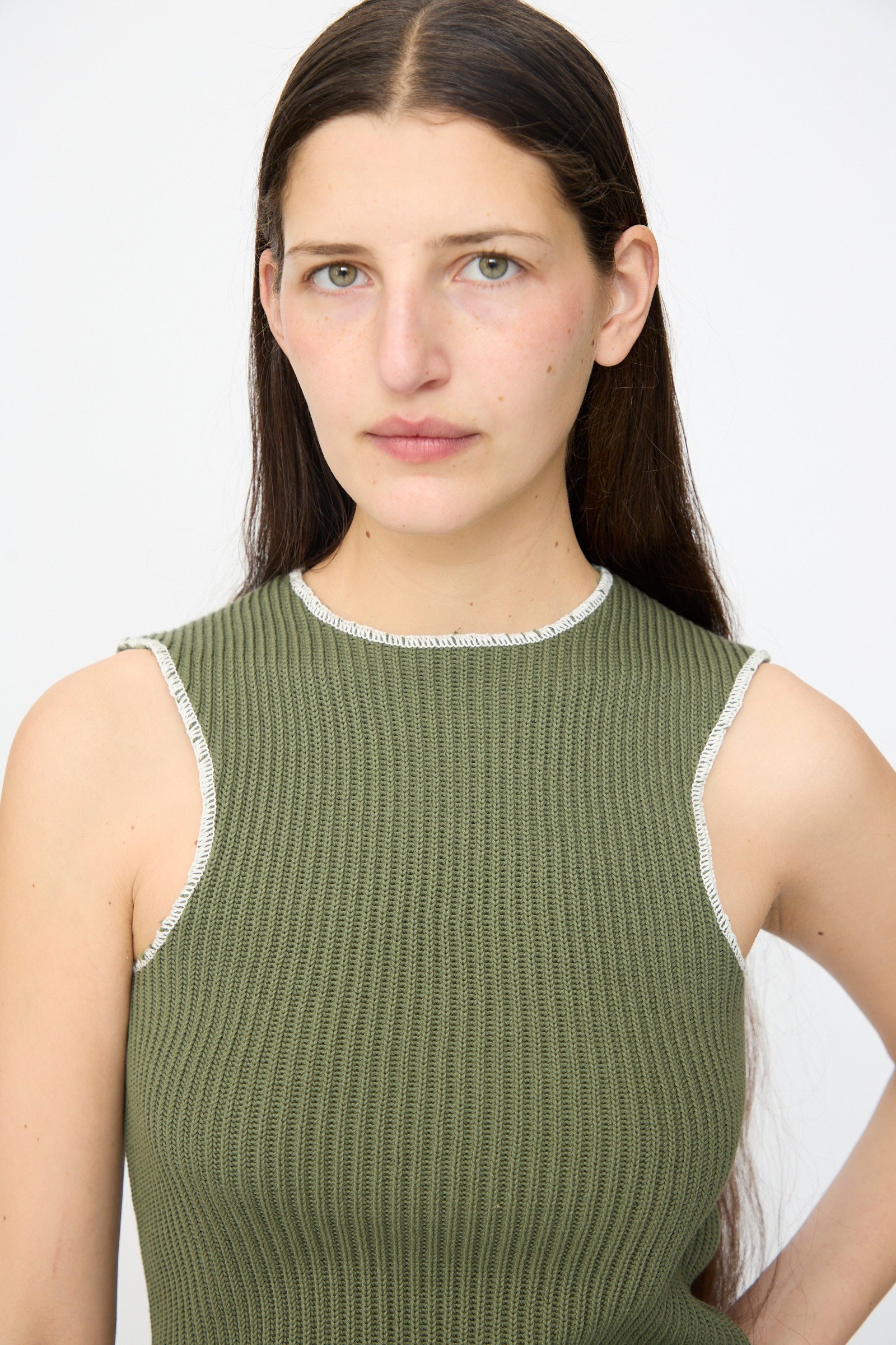 A person with long dark hair models the MM6 Top in Khaki, a slim fit ribbed tank, against a plain light background while looking directly at the camera.