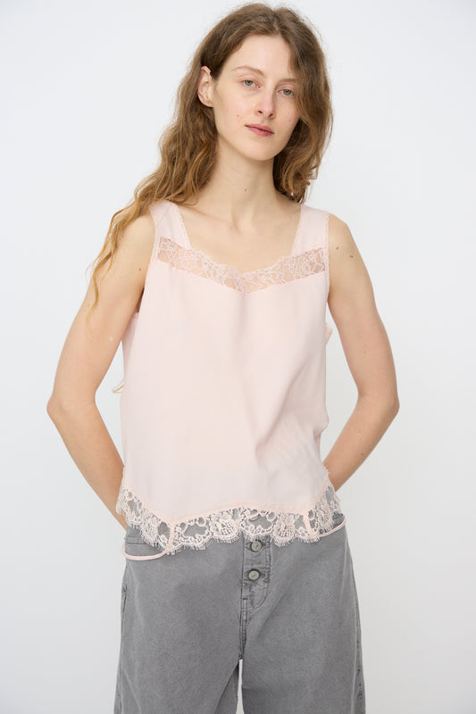 A person with long wavy hair wears the MM6 Top in Pink, a sleeveless lace trim camisole, paired with loose grey pants against a plain white background.