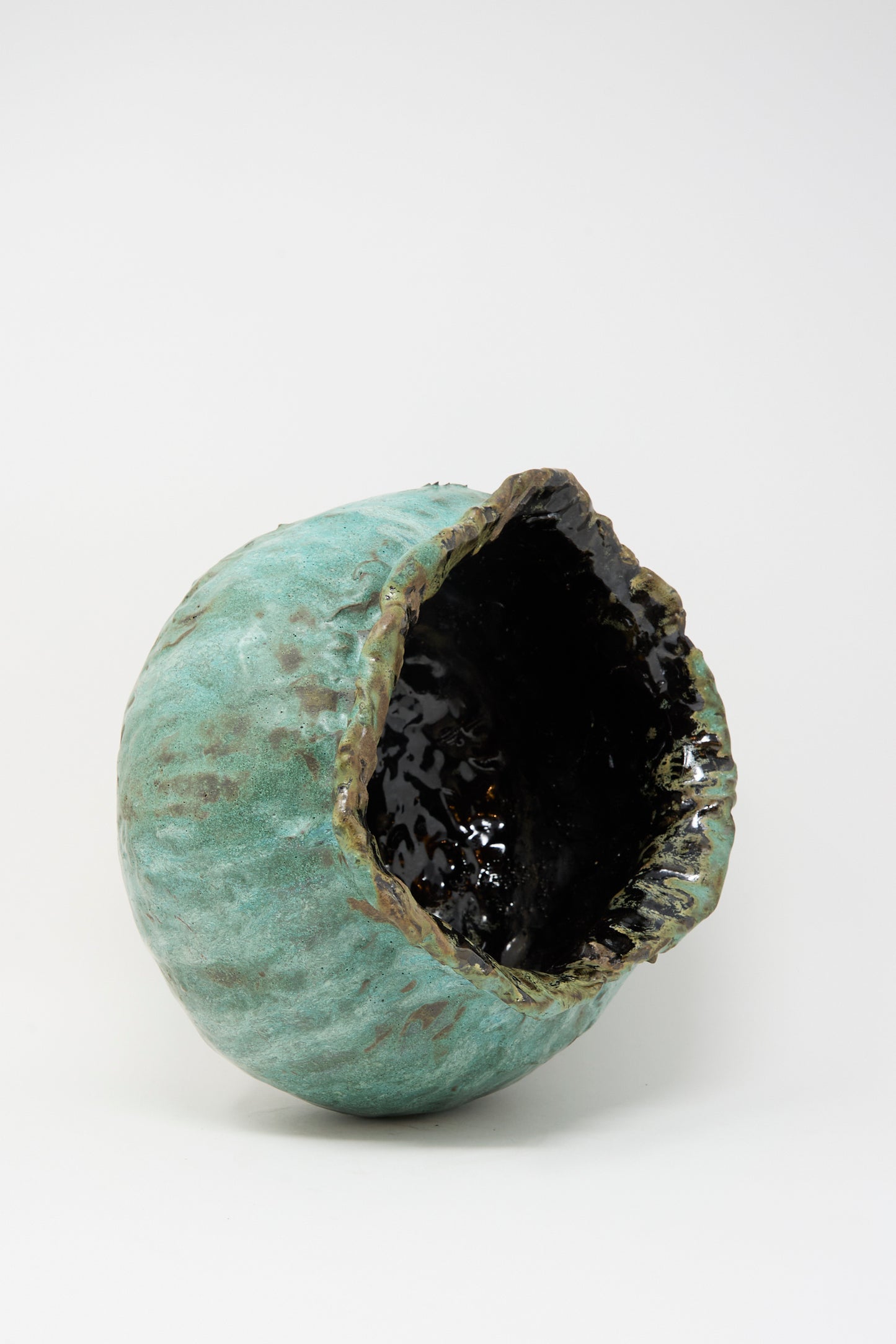 The MONDAYS Coiled Urn in Green is a round, textured stoneware piece with a matte green exterior and an irregular glossy black interior, shown against a plain white background.