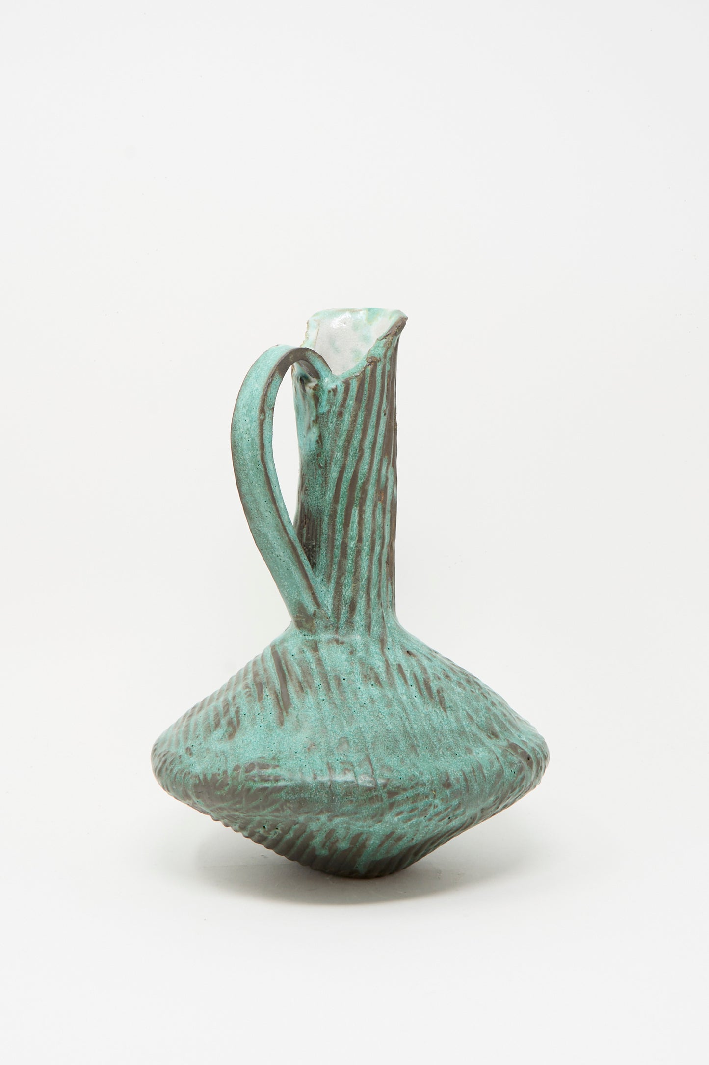 The MONDAYS Corrugated Pitcher in Green I is a textured, sculptural ceramic pitcher with a narrow neck, wide base, and curved handle, featuring a green glaze and photographed against a plain white background.