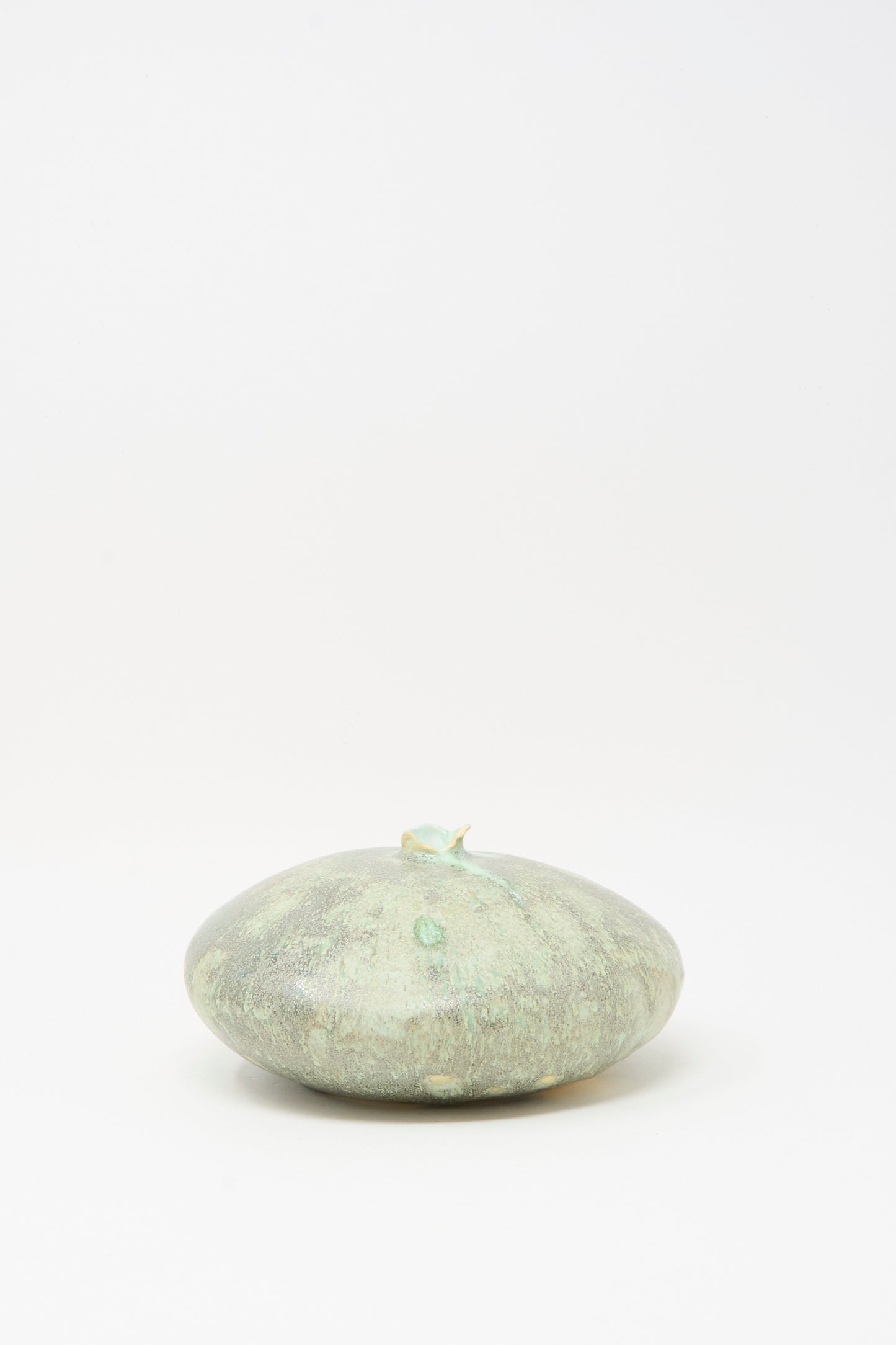 The MONDAYS Doyle Vase in Lichen, a round and flat piece with a short stem and smooth, light green surface, is centered on a plain white background, its glazed finish evoking the look of green clay.