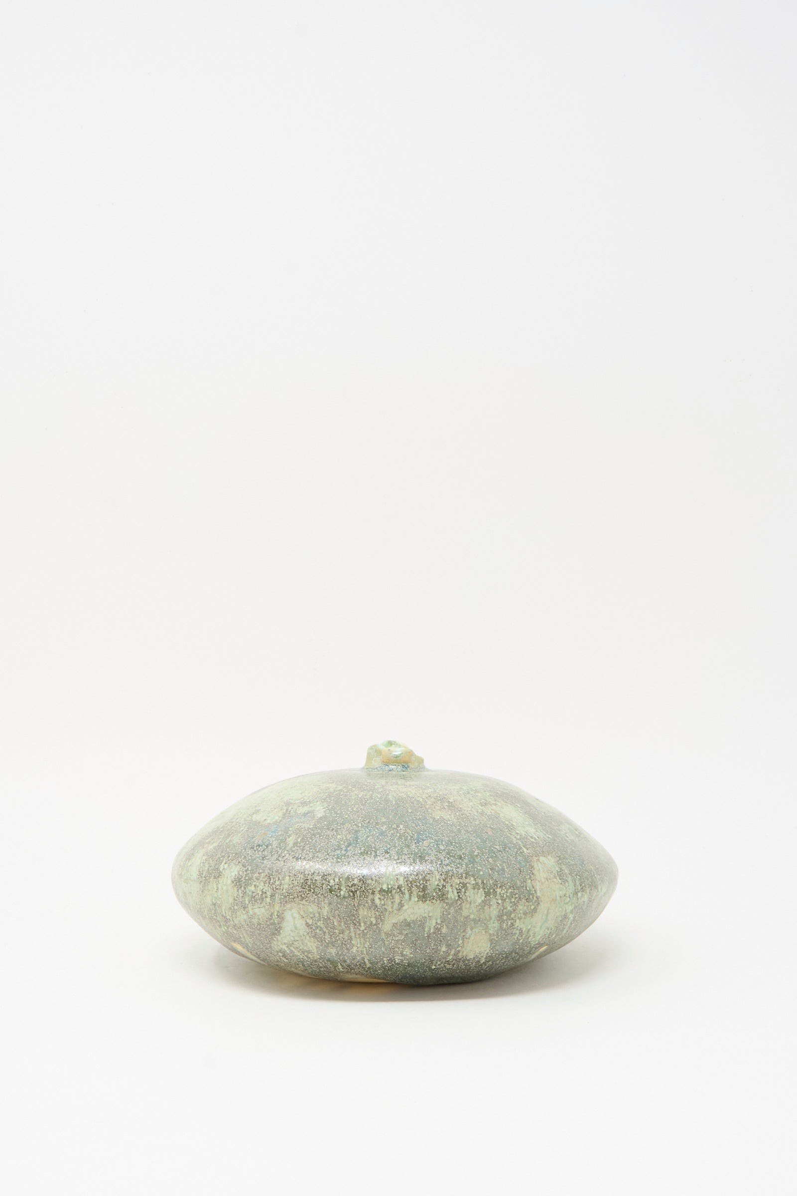 The Doyle Vase in Lichen by MONDAYS, a round, flat green glazed clay vase with a small top protrusion, is centered on a plain white background.