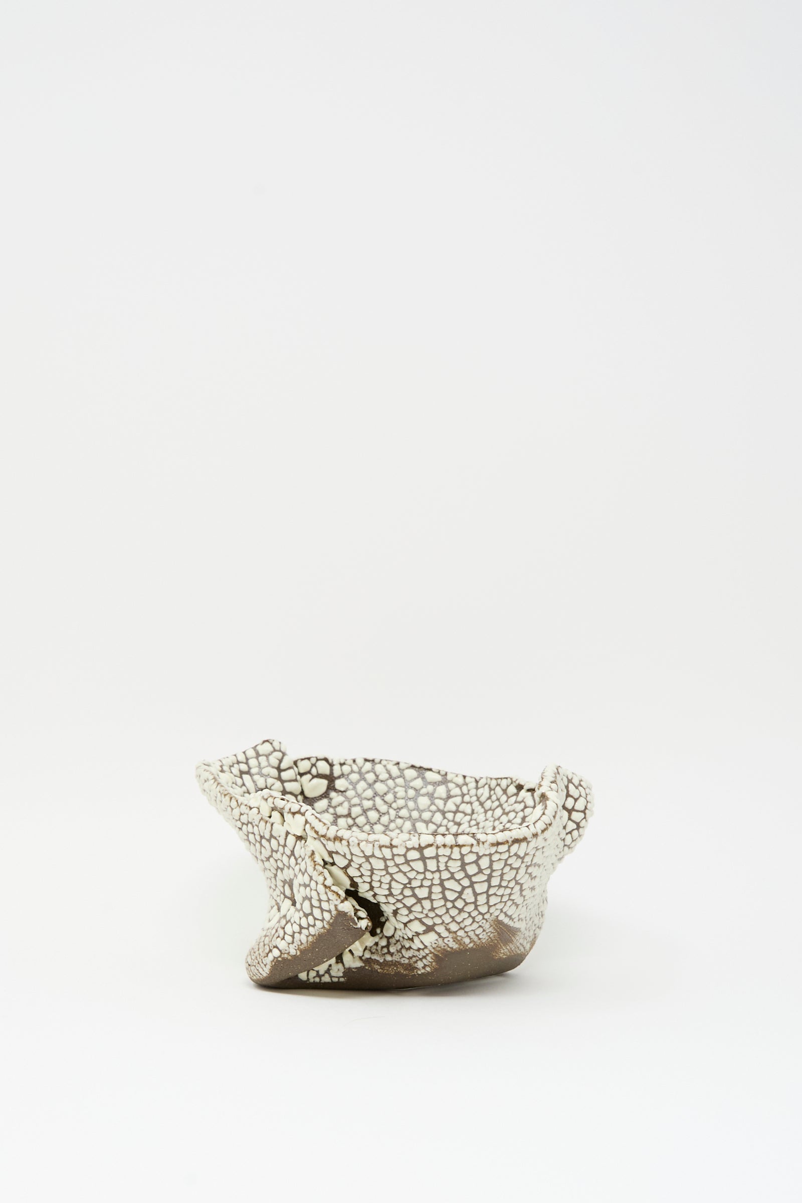 The Folded Bowl in Crawl II by MONDAYS features a cracked white glaze and rough edges, reflecting Brooklyn’s artisanal spirit against a simple white backdrop.