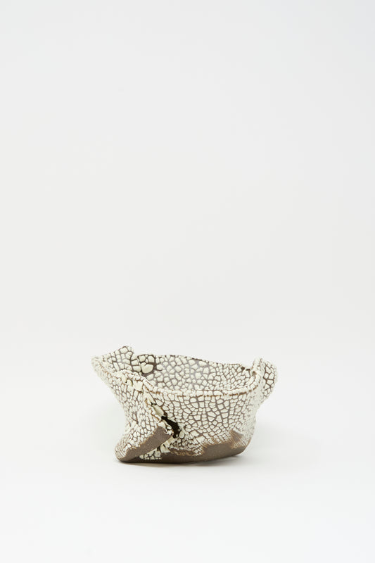 The Folded Bowl in Crawl II by MONDAYS features a cracked white glaze and rough edges, reflecting Brooklyn’s artisanal spirit against a simple white backdrop.