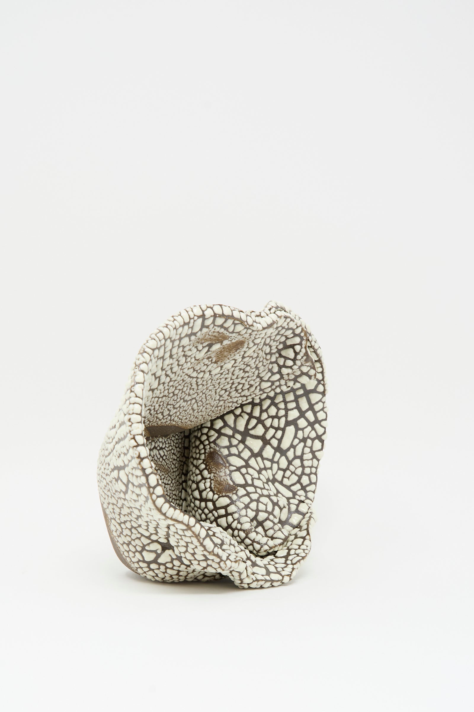 The Folded Bowl in Crawl III by MONDAYS is a ceramic, hand-built piece with a cracked, mosaic surface in white and brown and an irregular, folded shape shown against a plain white background.