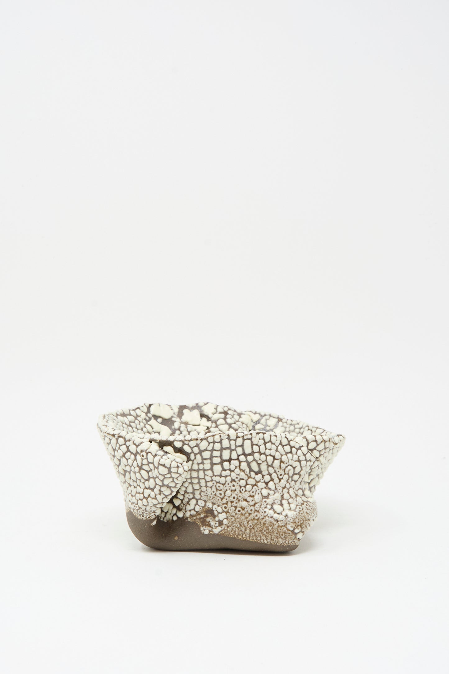 The MONDAYS Folded Wavy Bowl in Crawl II is a small, hand-built piece from Brooklyn featuring a textured crawling white glaze over a smooth brown base, shown on a plain white background.