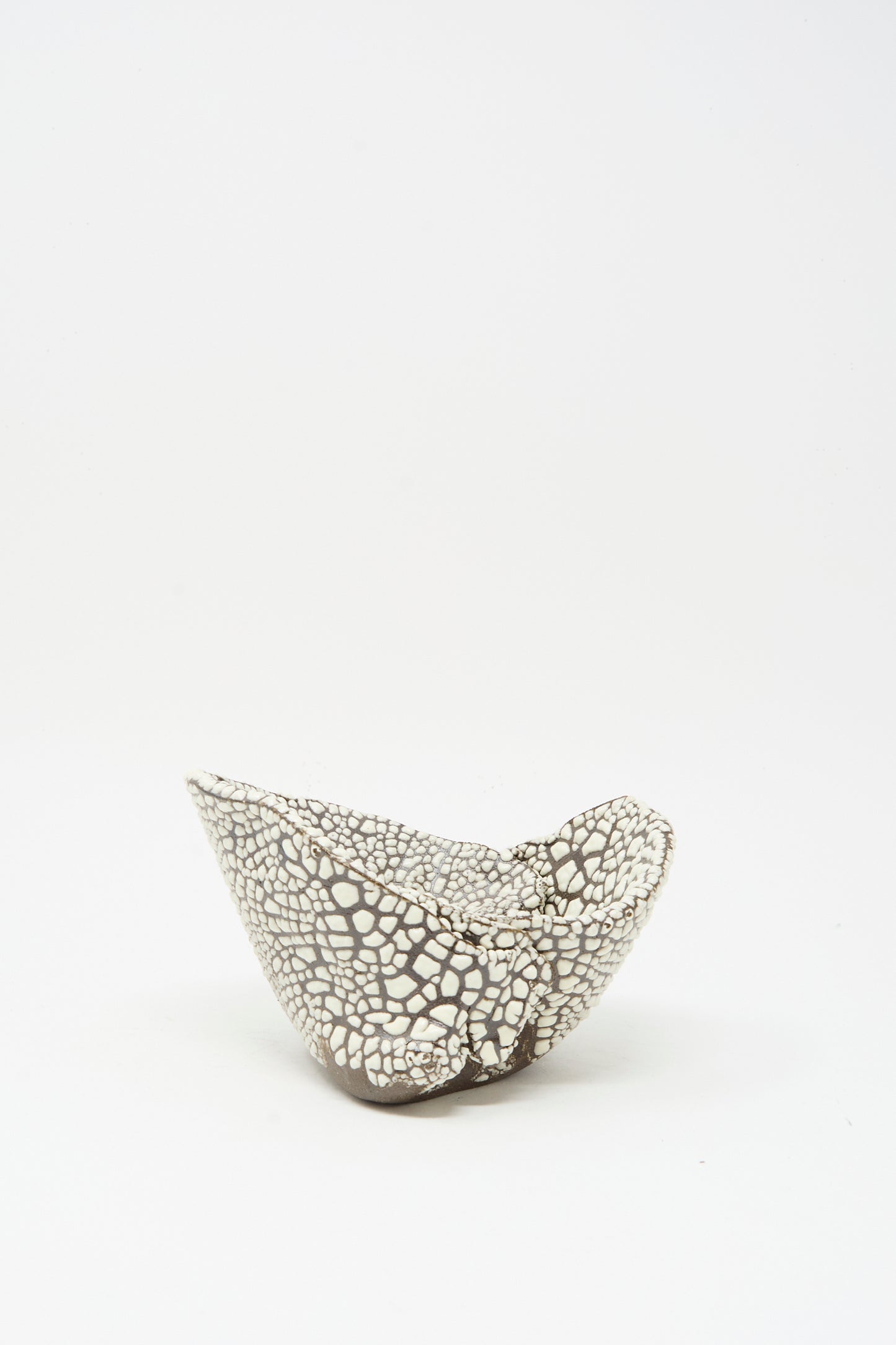 The Folded Wavy Bowl in Crawl III by MONDAYS features a small, asymmetrical hand-built shape with a black and white cracked pattern and glossy white glaze, showcasing Brooklyn’s modern ceramic style against a plain white background.