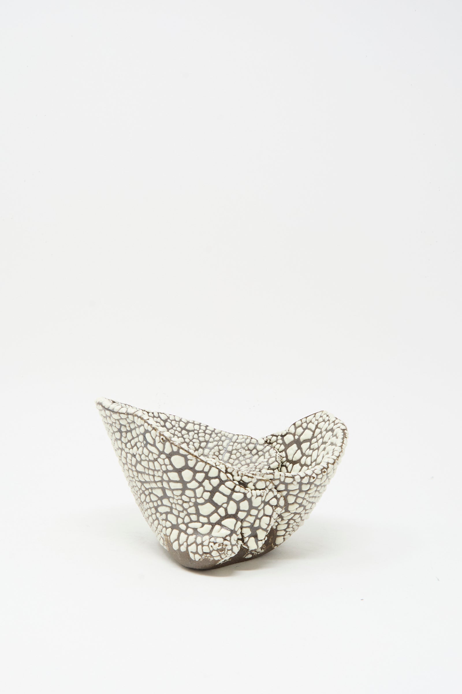 The Folded Wavy Bowl in Crawl III by MONDAYS features a small, asymmetrical hand-built shape with a black and white cracked pattern and glossy white glaze, showcasing Brooklyn’s modern ceramic style against a plain white background.