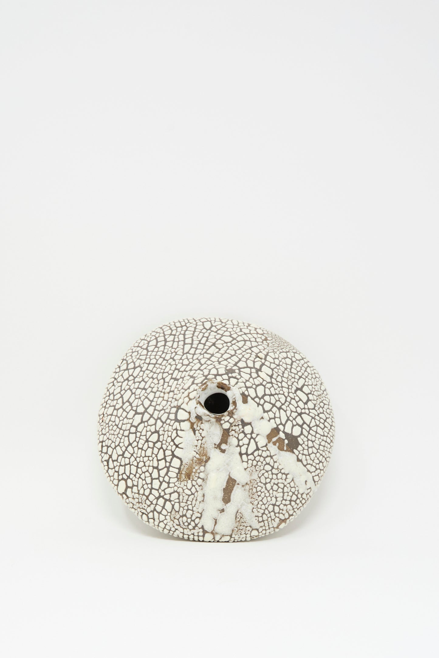 The MONDAYS Ikebana Vase in Crawl features a hand-built, round flat shape with a small central opening, showcasing a crawling white glaze over crackled brown clay, set against a plain white background.