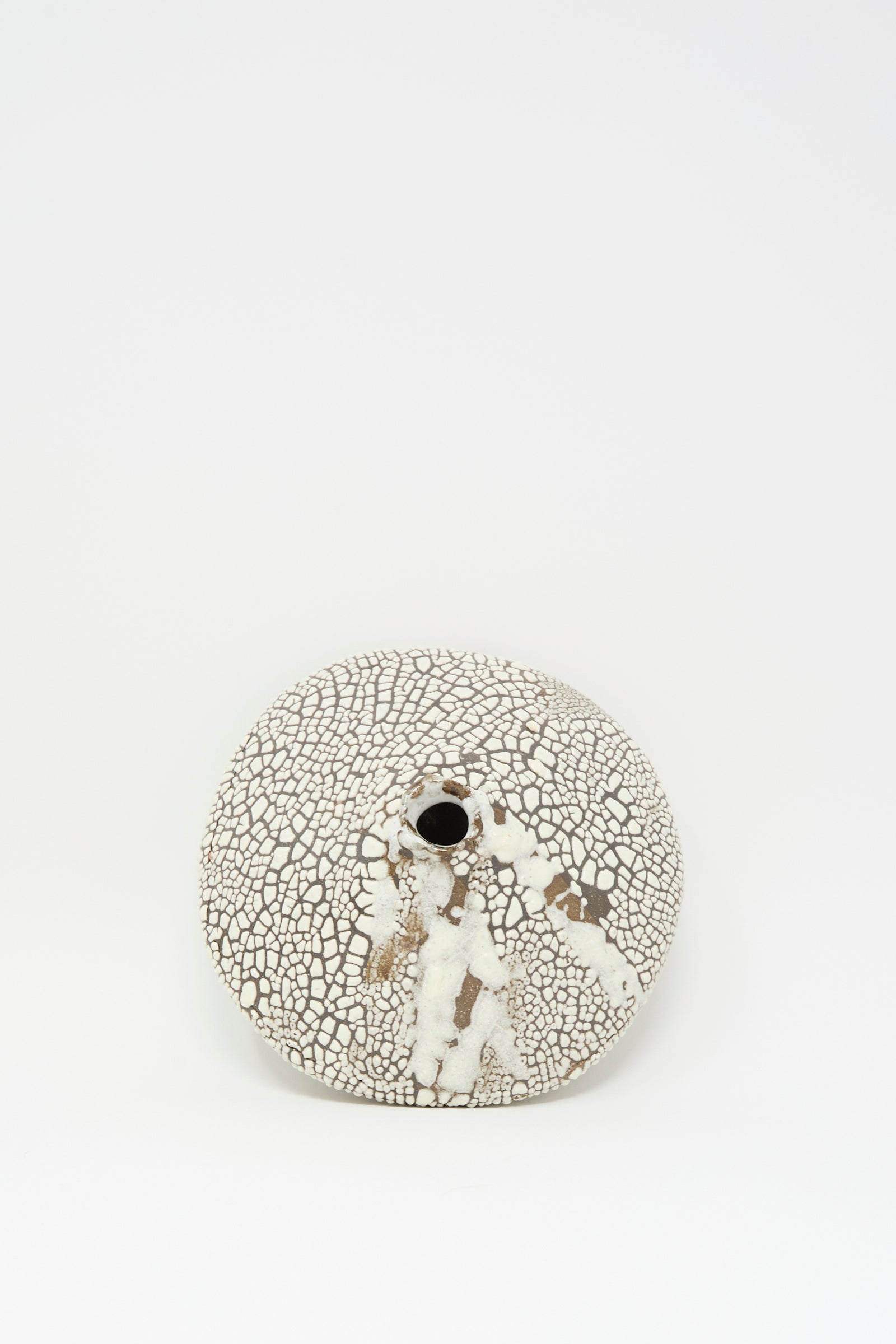 The MONDAYS Ikebana Vase in Crawl features a hand-built, round flat shape with a small central opening, showcasing a crawling white glaze over crackled brown clay, set against a plain white background.