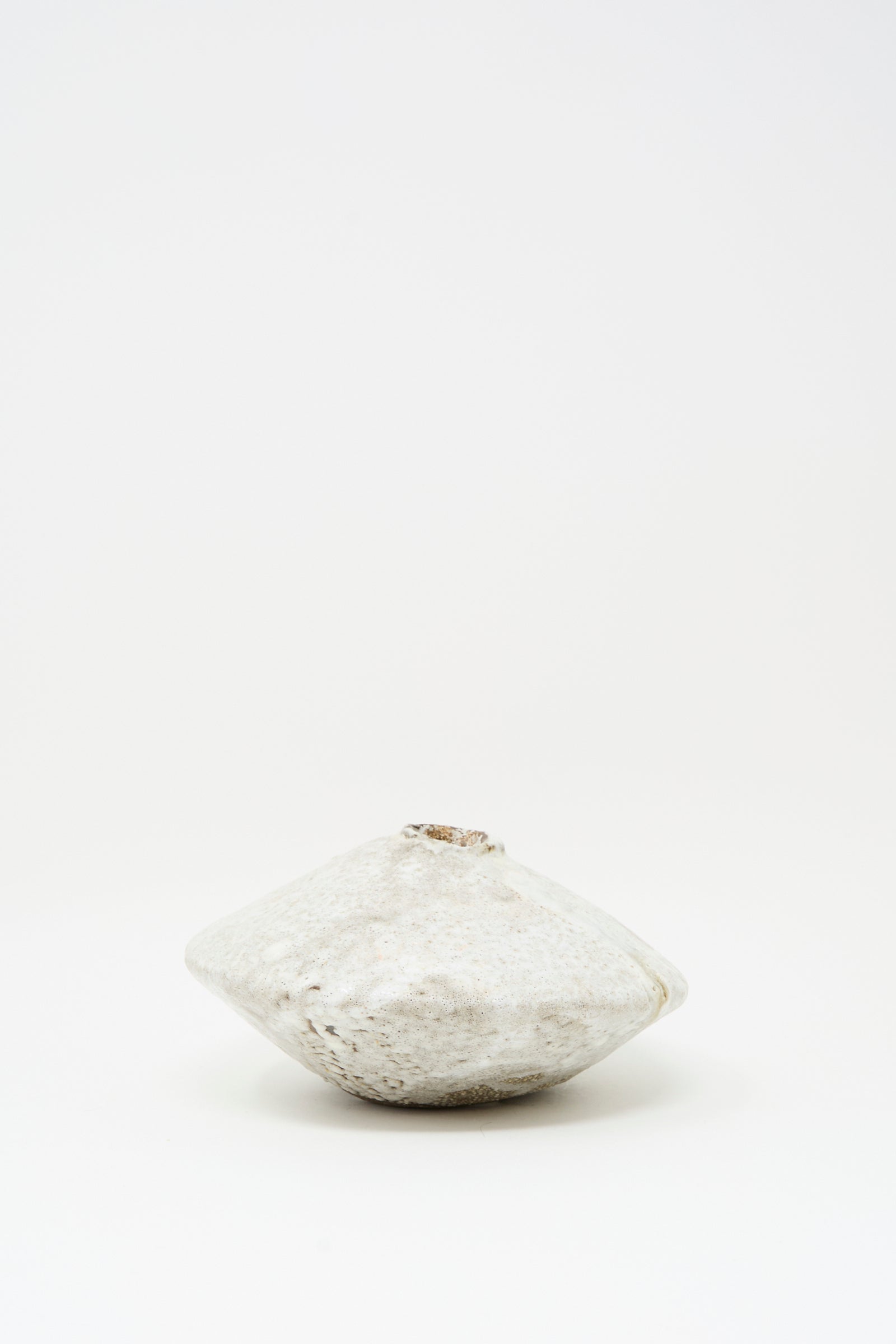 The MONDAYS Ikebana Vase in White over Dark Brown features a round, flat shape with a rough texture and subtle white glaze, evoking minimalist elegance against a plain white background.