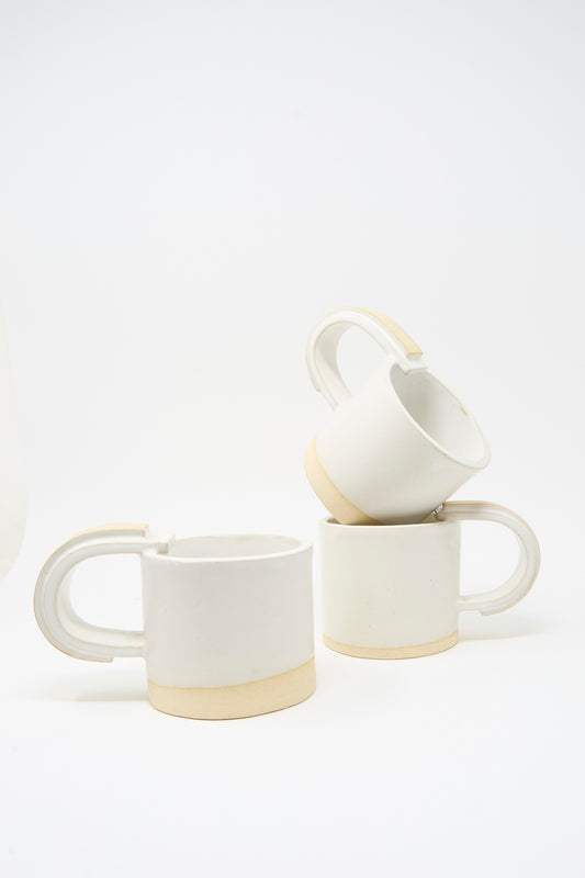 Three MONDAYS Layered Mugs in White on Sand are stacked on a plain white background, each with a beige base and unglazed handle that highlight their unique, handmade feel.