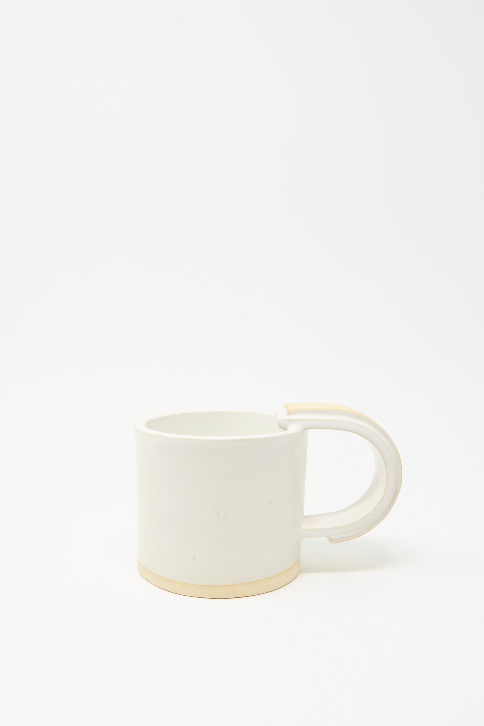 The MONDAYS Layered Mug in White on Sand features a handmade, slab-built design with a white ceramic body, rounded handle, and unglazed beige base, shown against a white background.