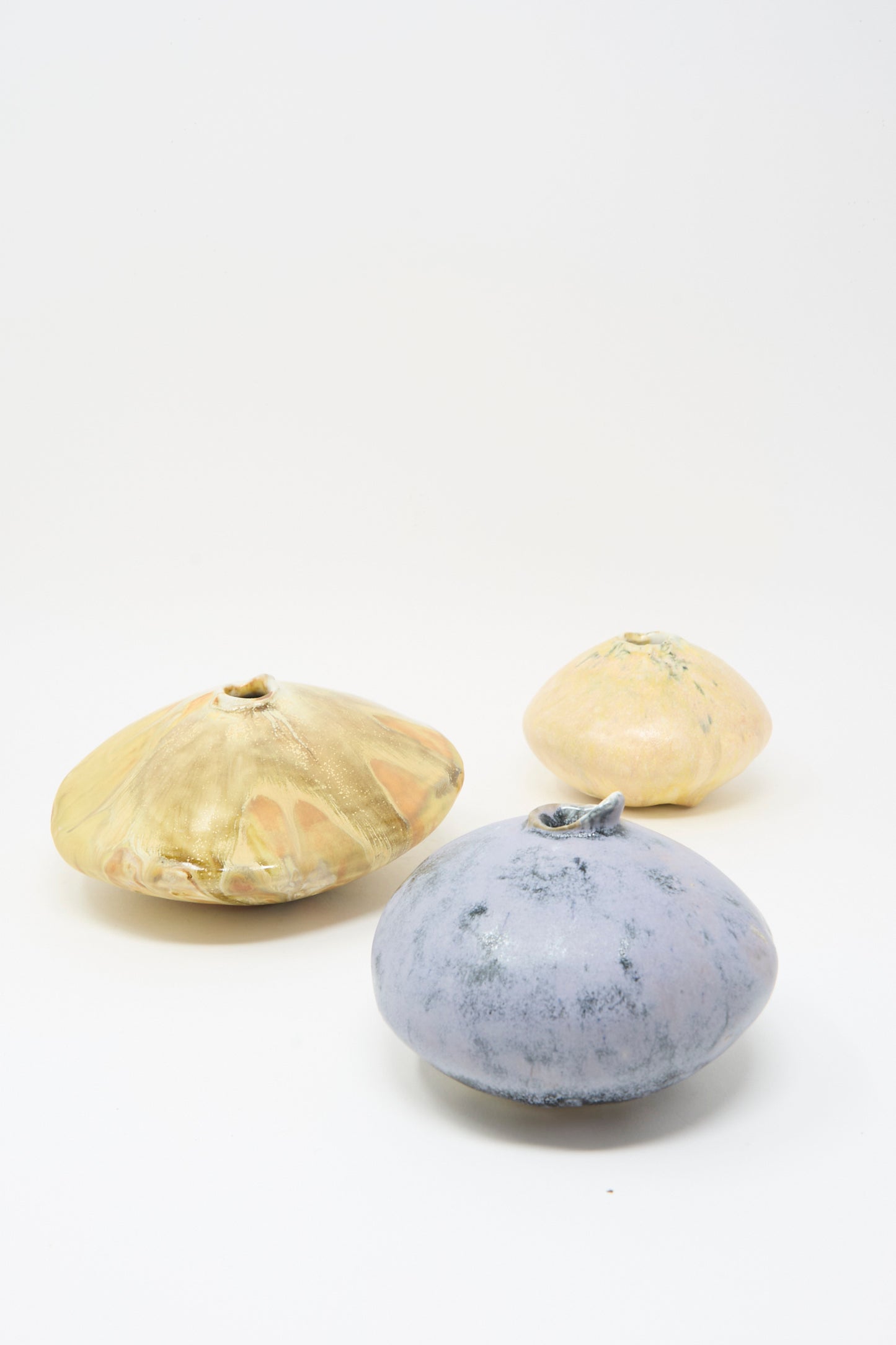 The MONDAYS Mini Moon Vase in Yellow Multi—a round, flat, handmade stoneware vase—adds Upstate NY artistry to your space. Shown on a white background alongside peach and blue styles.