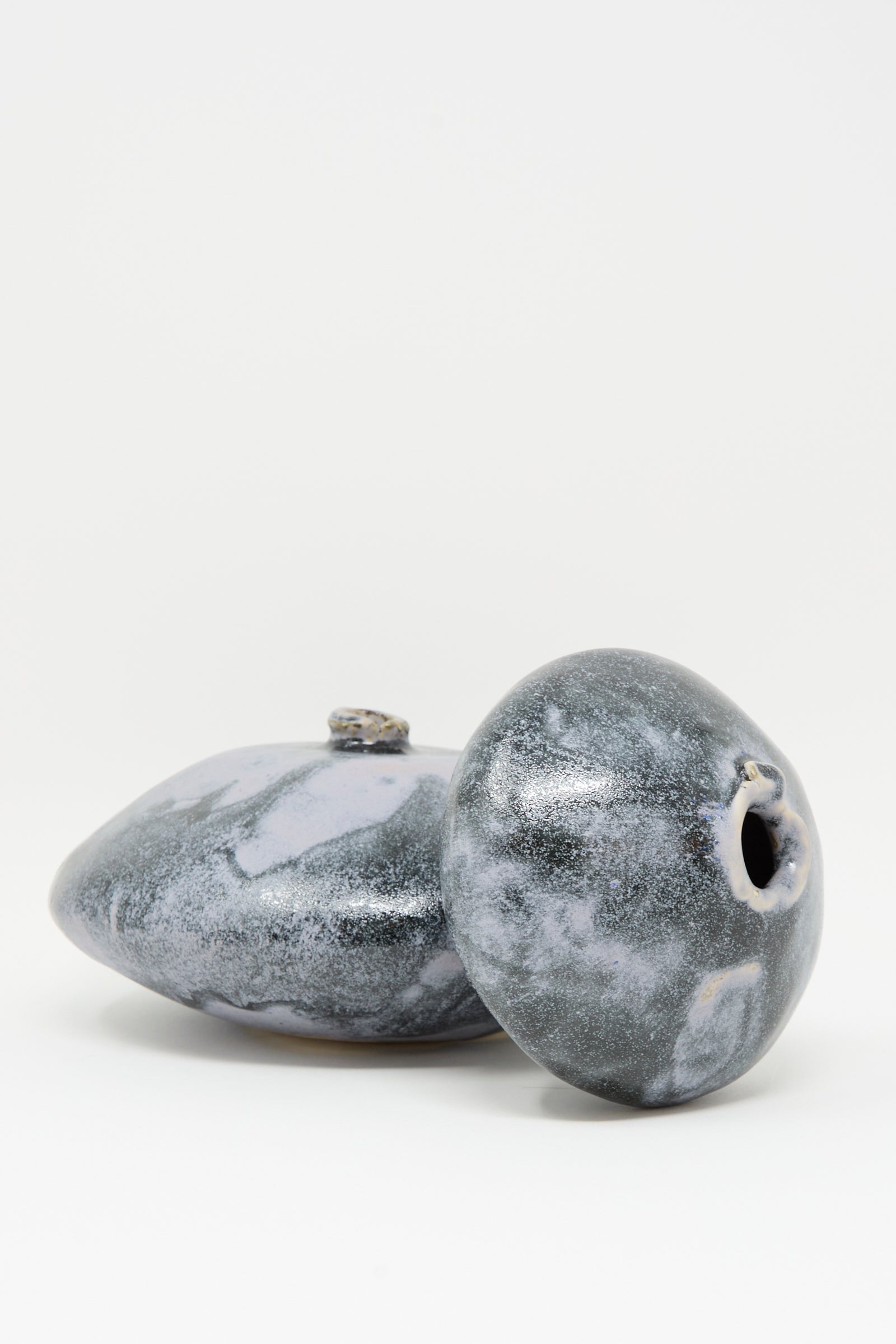 Two round, smooth MONDAYS Moon Vase in Storm ceramics with gray and white marbled patterns are positioned on a plain white background—one upright, one lying on its side.