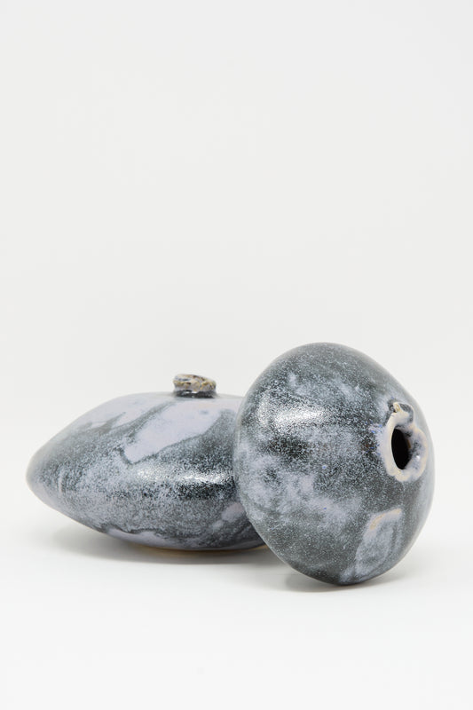 Two round, smooth MONDAYS Moon Vase in Storm ceramics with gray and white marbled patterns are positioned on a plain white background—one upright, one lying on its side.