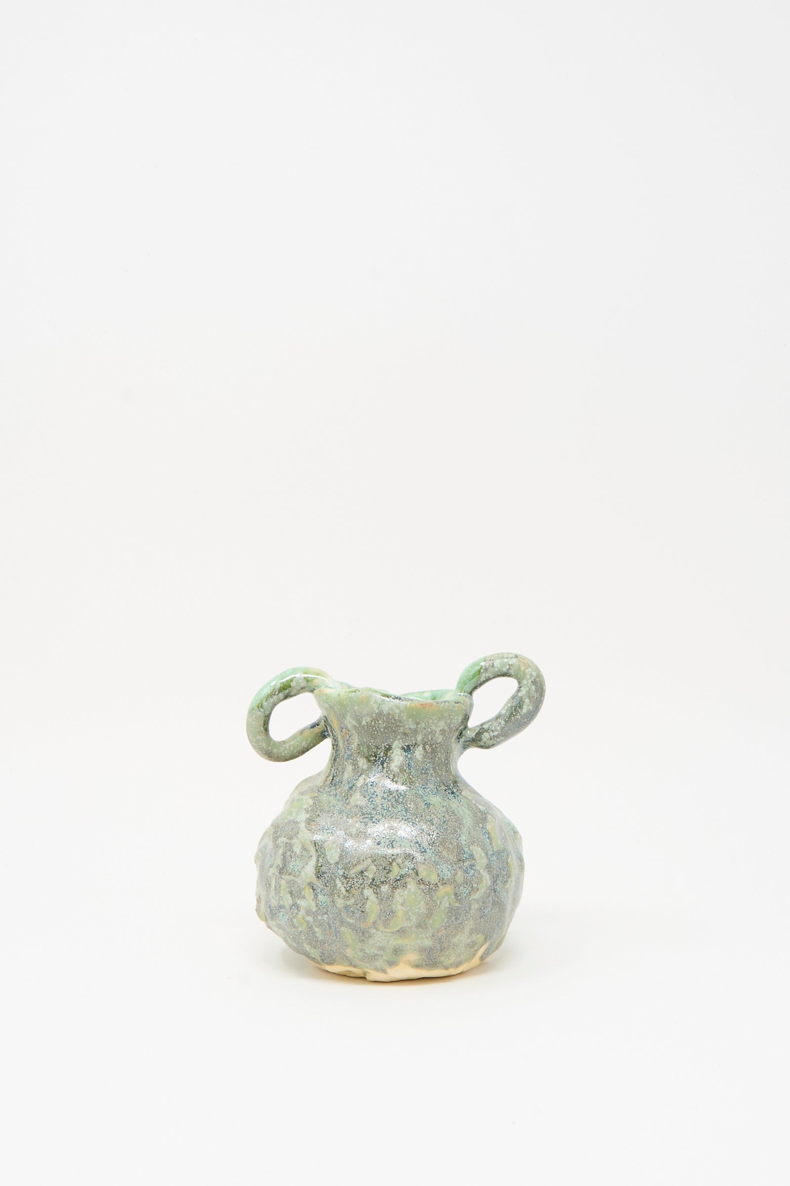 The MONDAYS Pinched Vase with Handles in Green features a handmade ceramic design and mottled glaze, standing out beautifully against a plain white background.