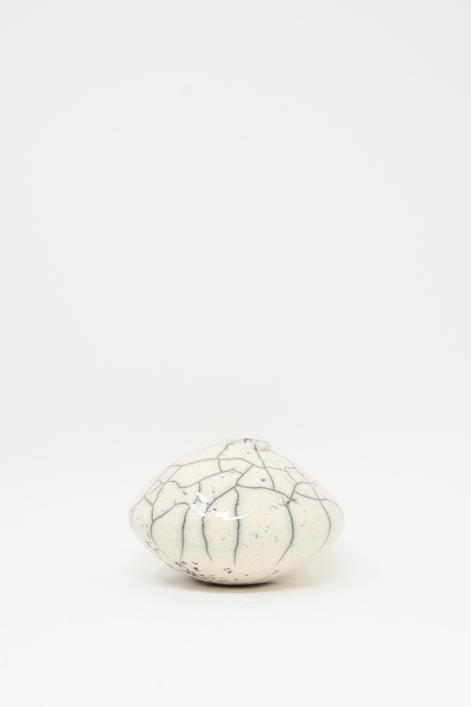 The MONDAYS Raku Moon Vase in White is a small, round ceramic piece with dark, irregular crackle lines, set against a plain white background.