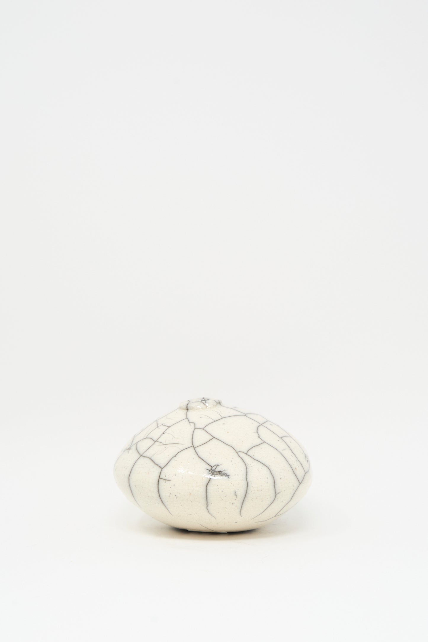 The MONDAYS Raku Moon Vase in White, a small round ceramic piece with dark crackle patterns and a subtle white glaze, is centered on a plain white background.