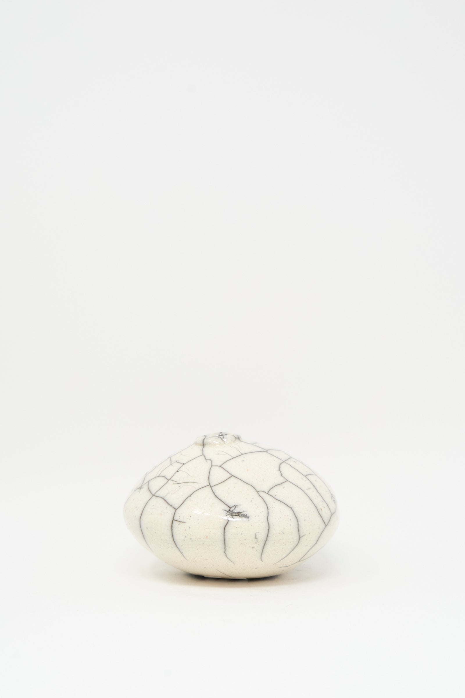 The MONDAYS Raku Moon Vase in White, a small round ceramic piece with dark crackle patterns and a subtle white glaze, is centered on a plain white background.