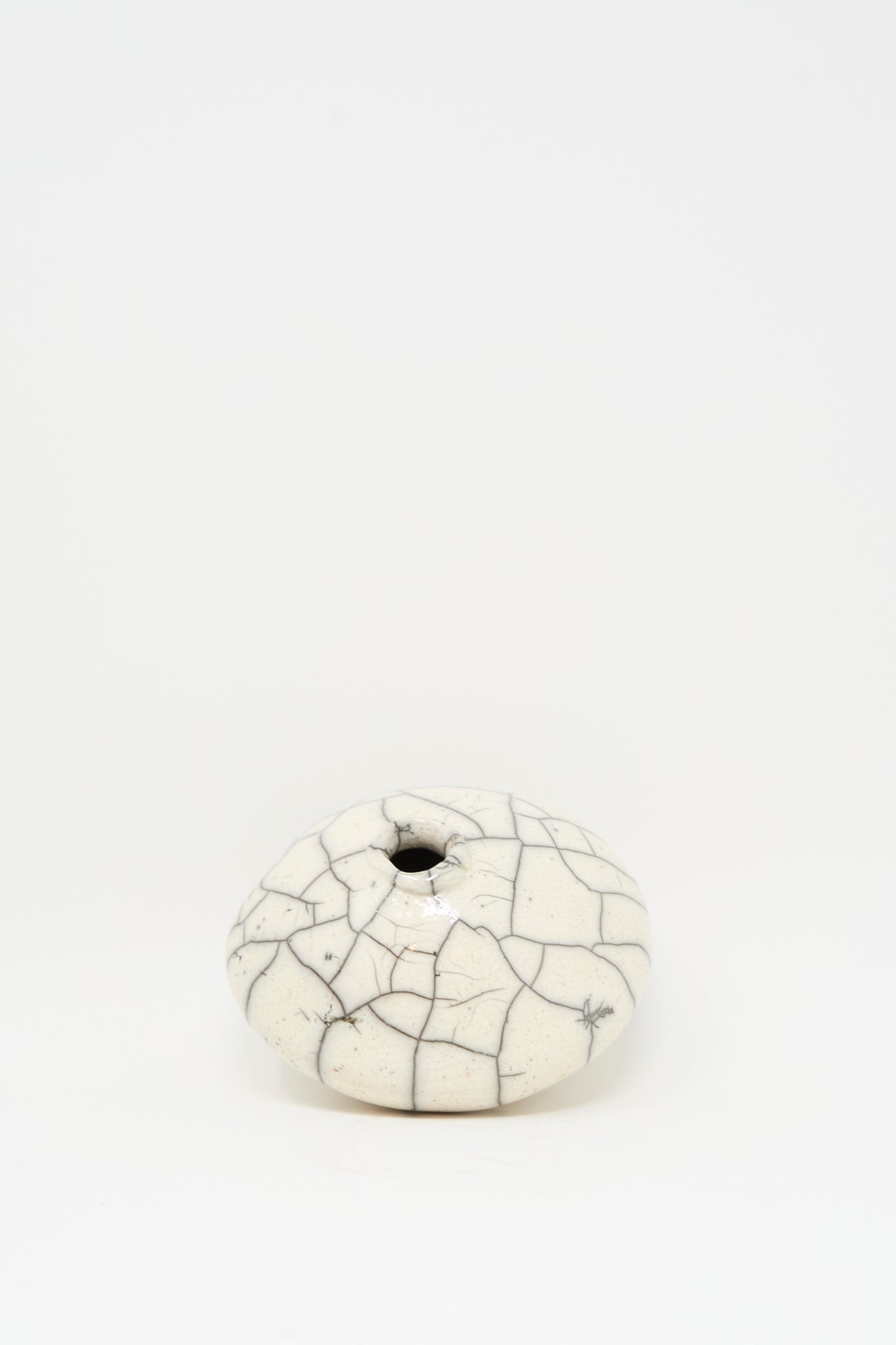 The Raku Moon Vase in White by MONDAYS is a small, round stoneware piece with a narrow opening and white crackle glaze, shown elegantly on a plain white background.