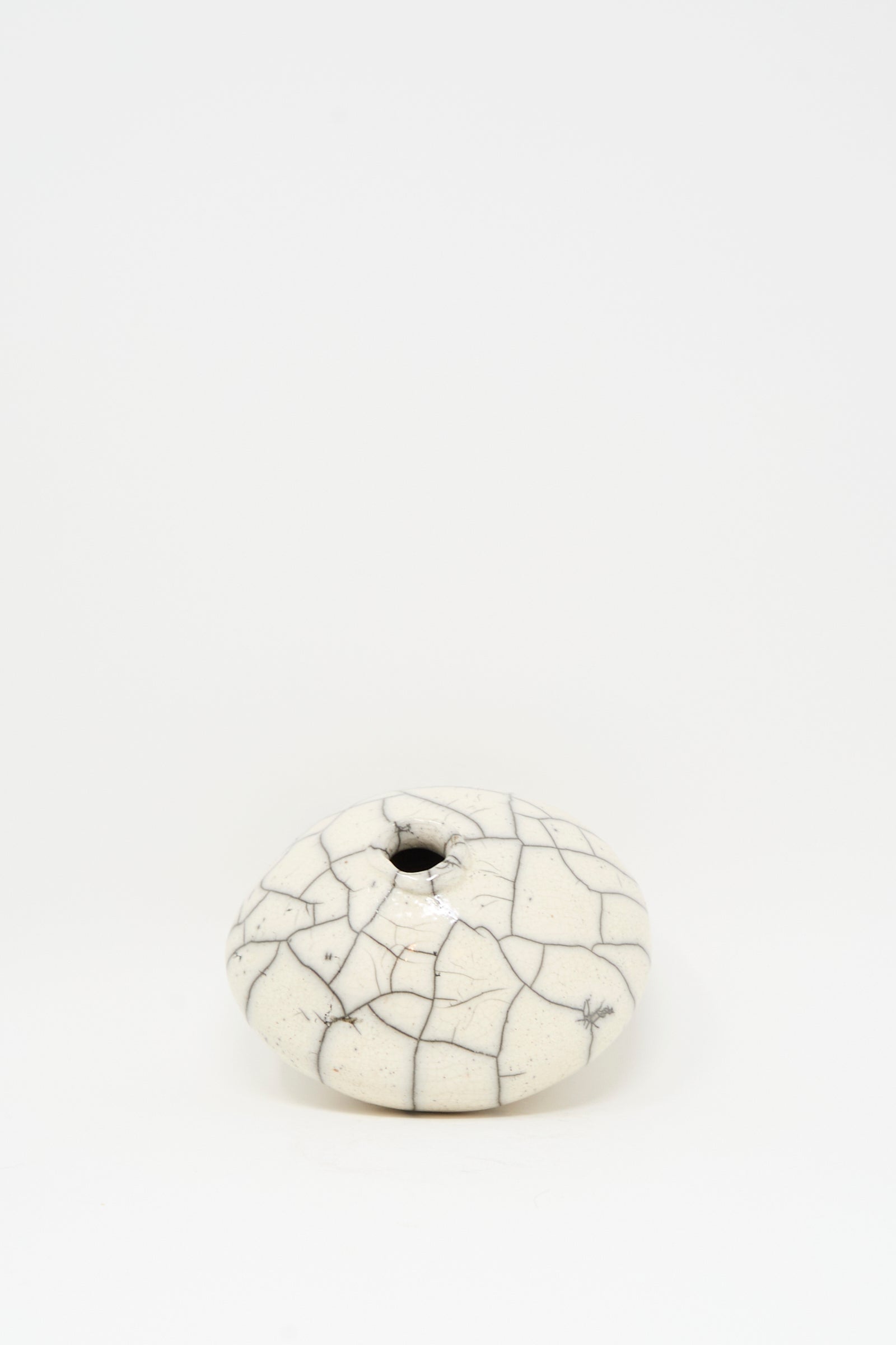 The Raku Moon Vase in White by MONDAYS is a small, round stoneware piece with a narrow opening and white crackle glaze, shown elegantly on a plain white background.