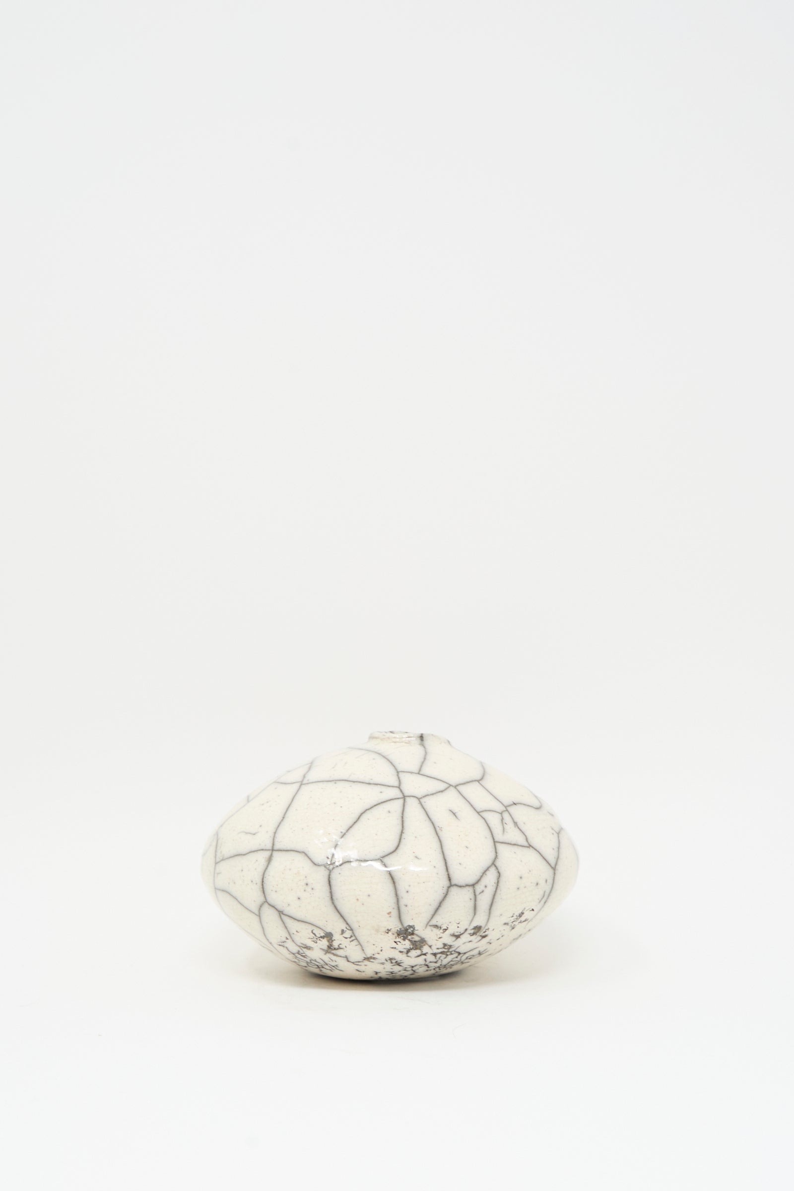The Raku Moon Vase in White by MONDAYS is a round, white stoneware vase with a narrow opening and bold black crackle pattern, shown on a plain white background.