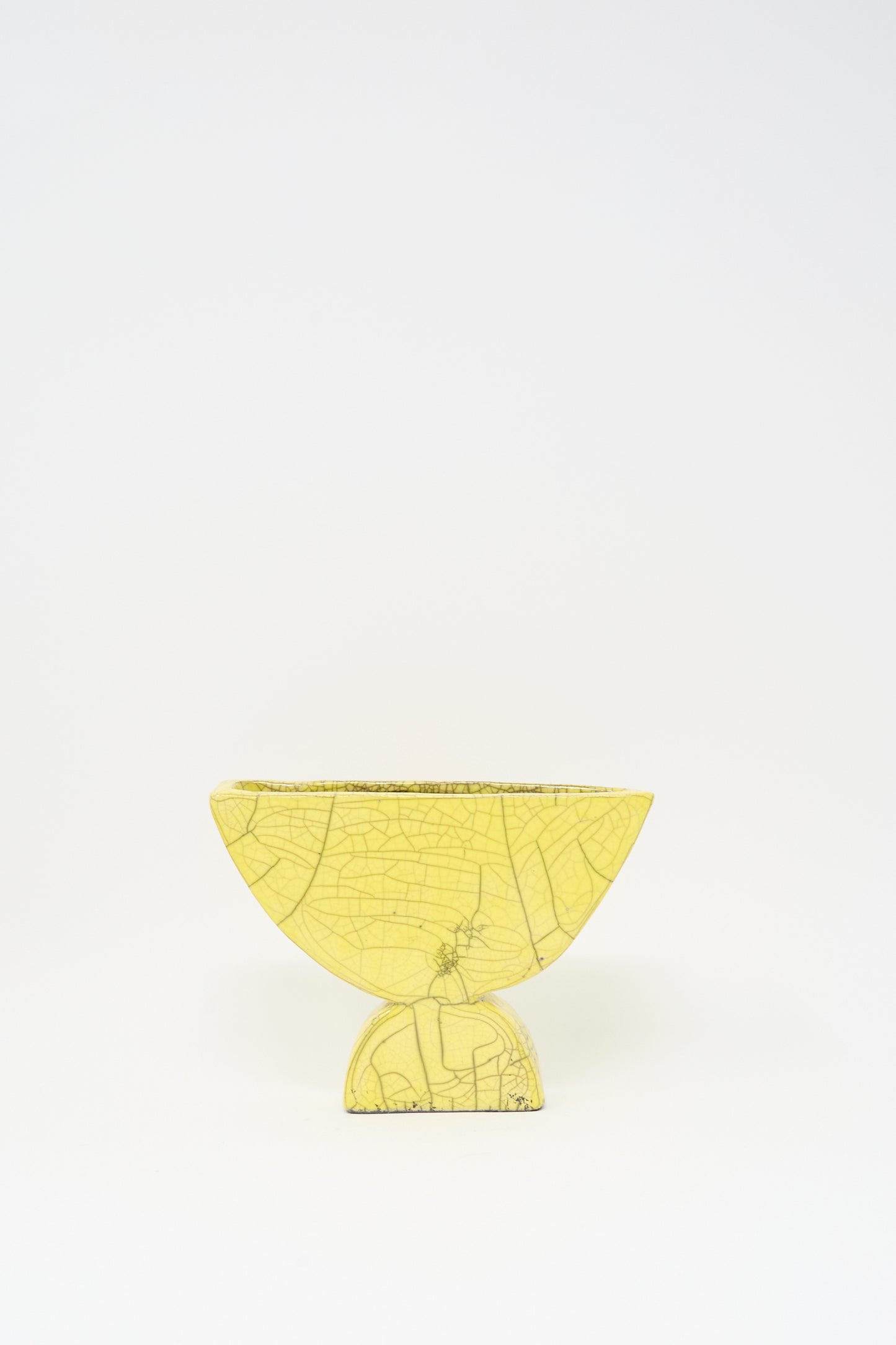 The MONDAYS Raku Semicircle Vessel in Yellow, a small semi-circular vase with visible crackle lines, sits on a matching round base against a plain white background.