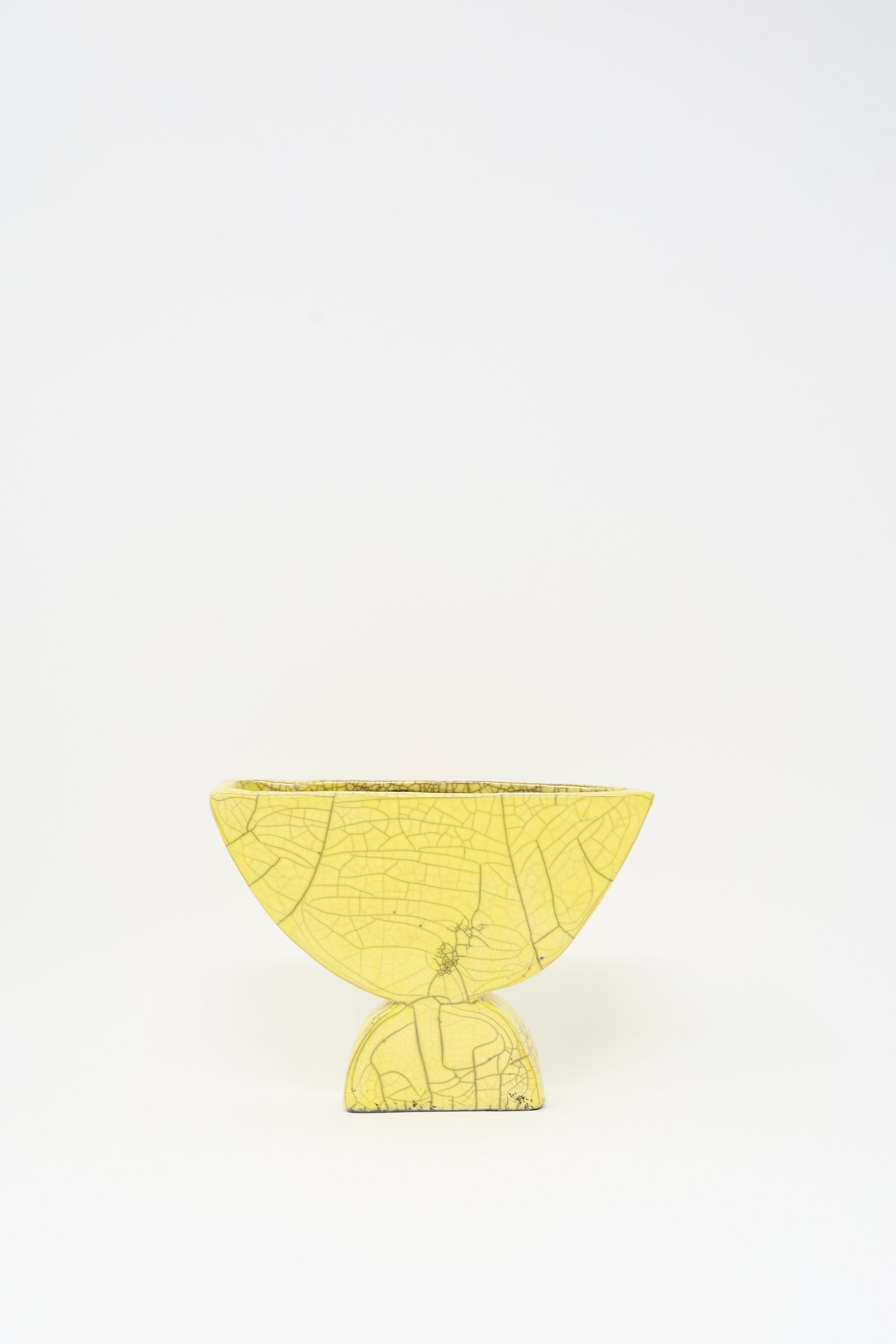 The MONDAYS Raku Semicircle Vessel in Yellow, a small semi-circular vase with visible crackle lines, sits on a matching round base against a plain white background.
