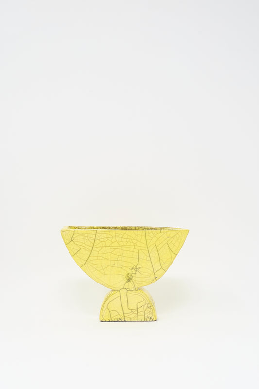 The MONDAYS Raku Semicircle Vessel in Yellow, a small semi-circular vase with visible crackle lines, sits on a matching round base against a plain white background.