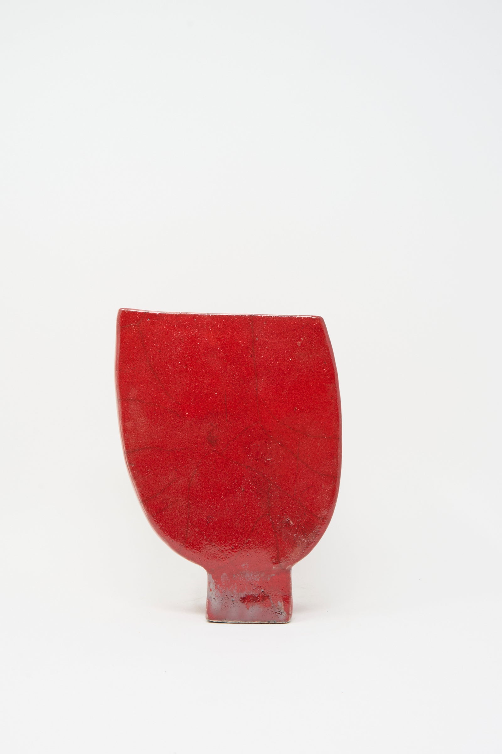 The MONDAYS Raku Vessel in Red is a handmade vase featuring a flat bottom, curved top, and rectangular base, displayed against a plain white background.