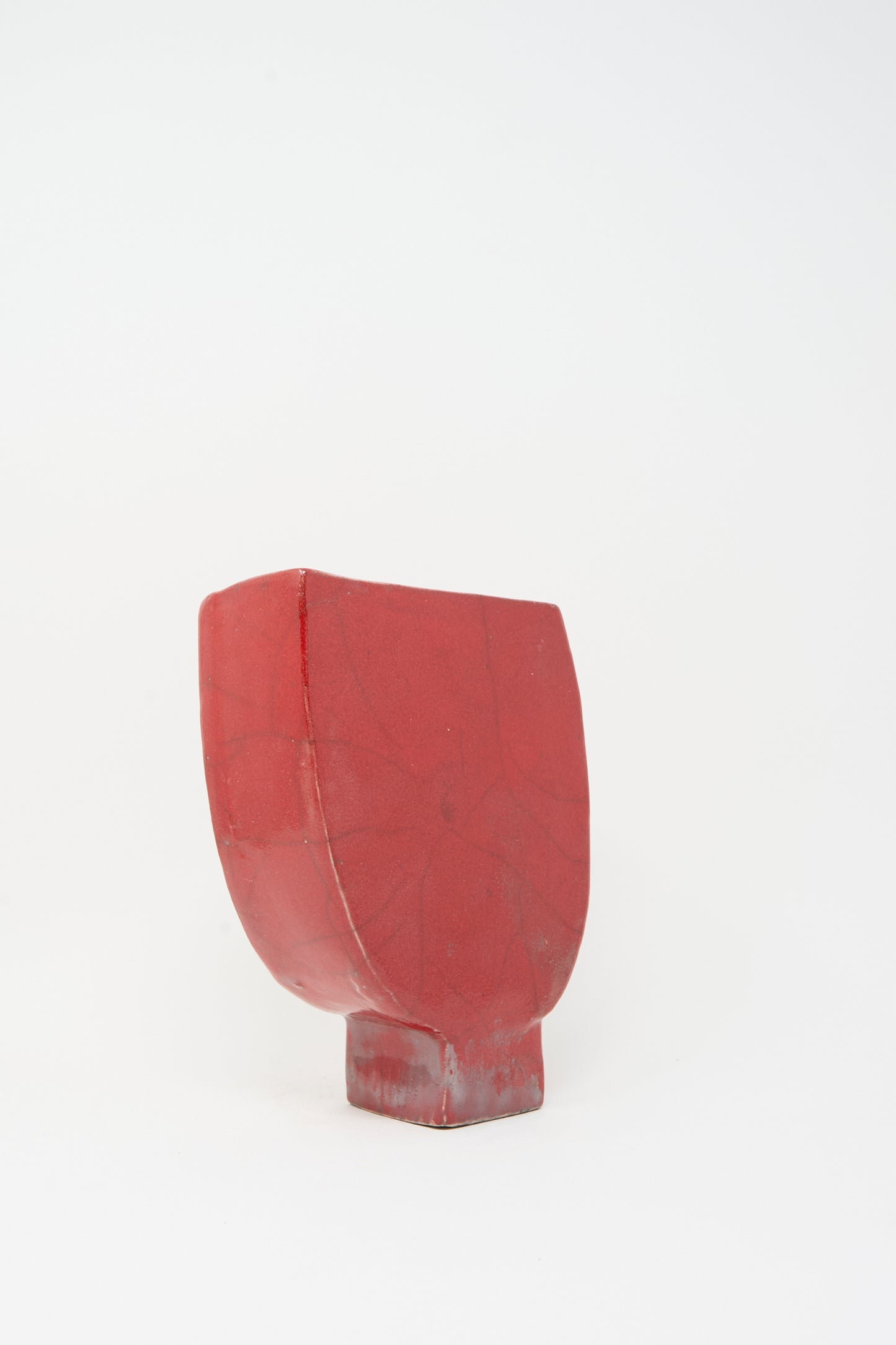 The MONDAYS Raku Vessel in Red is a handmade geometric vase with a matte finish and subtle vein-like lines, standing upright on a small rectangular base against a plain white background.