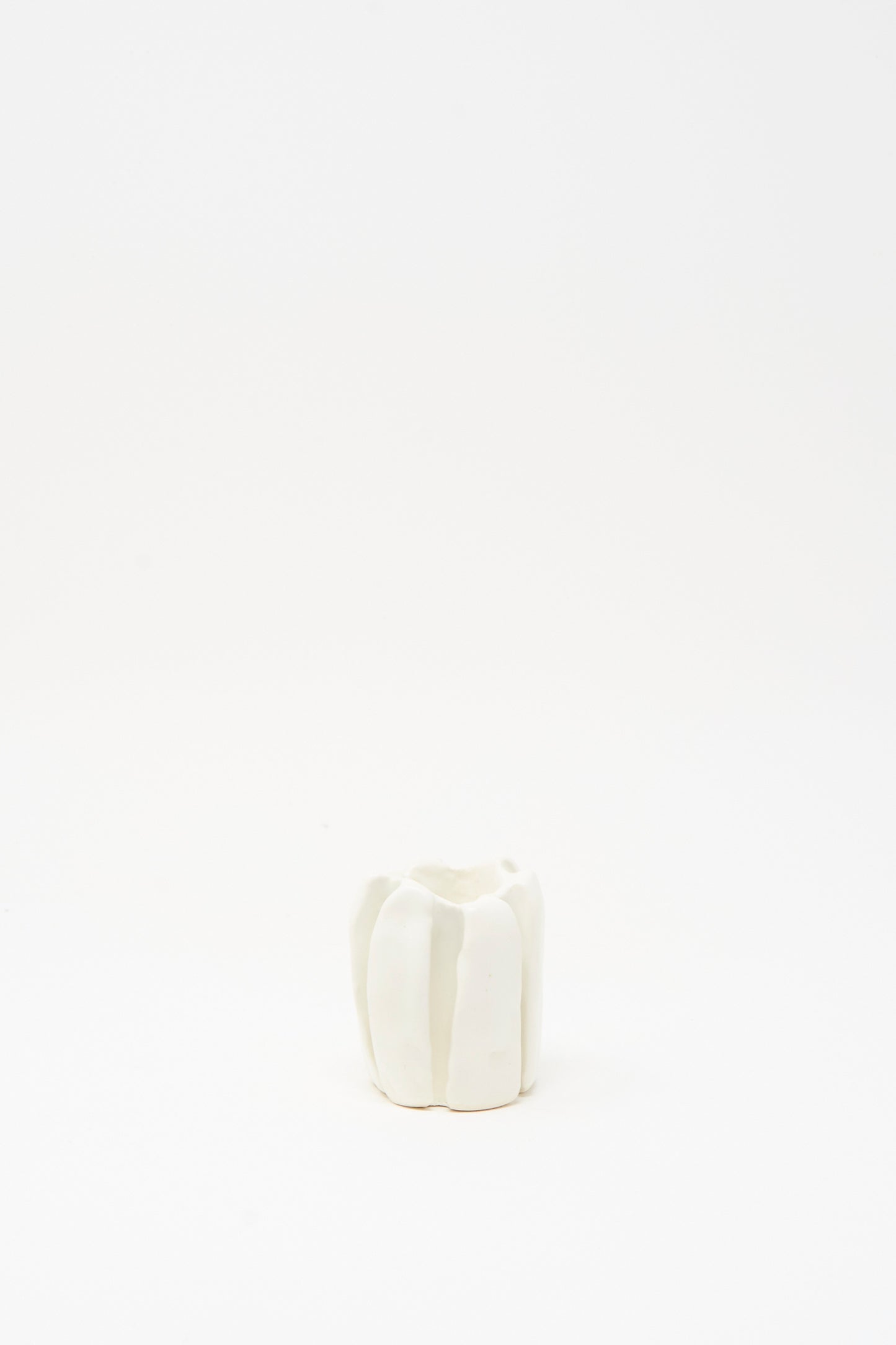 The MONDAYS Ribbed Candleholder in White, featuring vertical grooves and crafted from porcelain, is centered on a plain white background.
