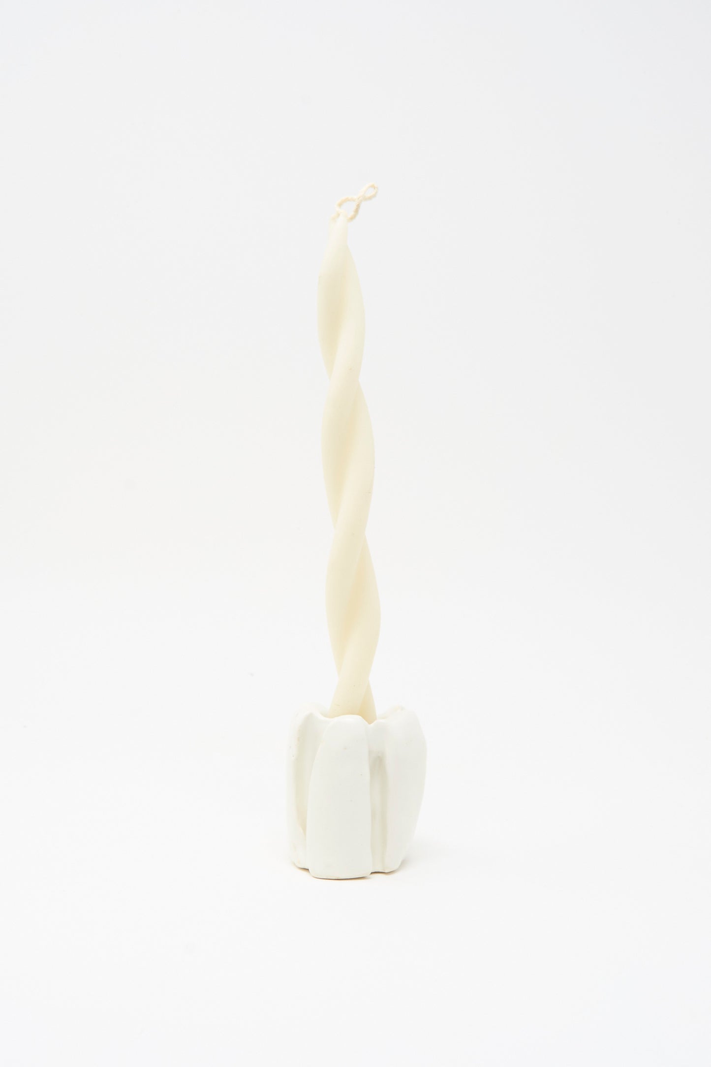 A twisted white candle stands upright in the MONDAYS Ribbed Candleholder in White, handmade in Brooklyn, set against a plain white background.
