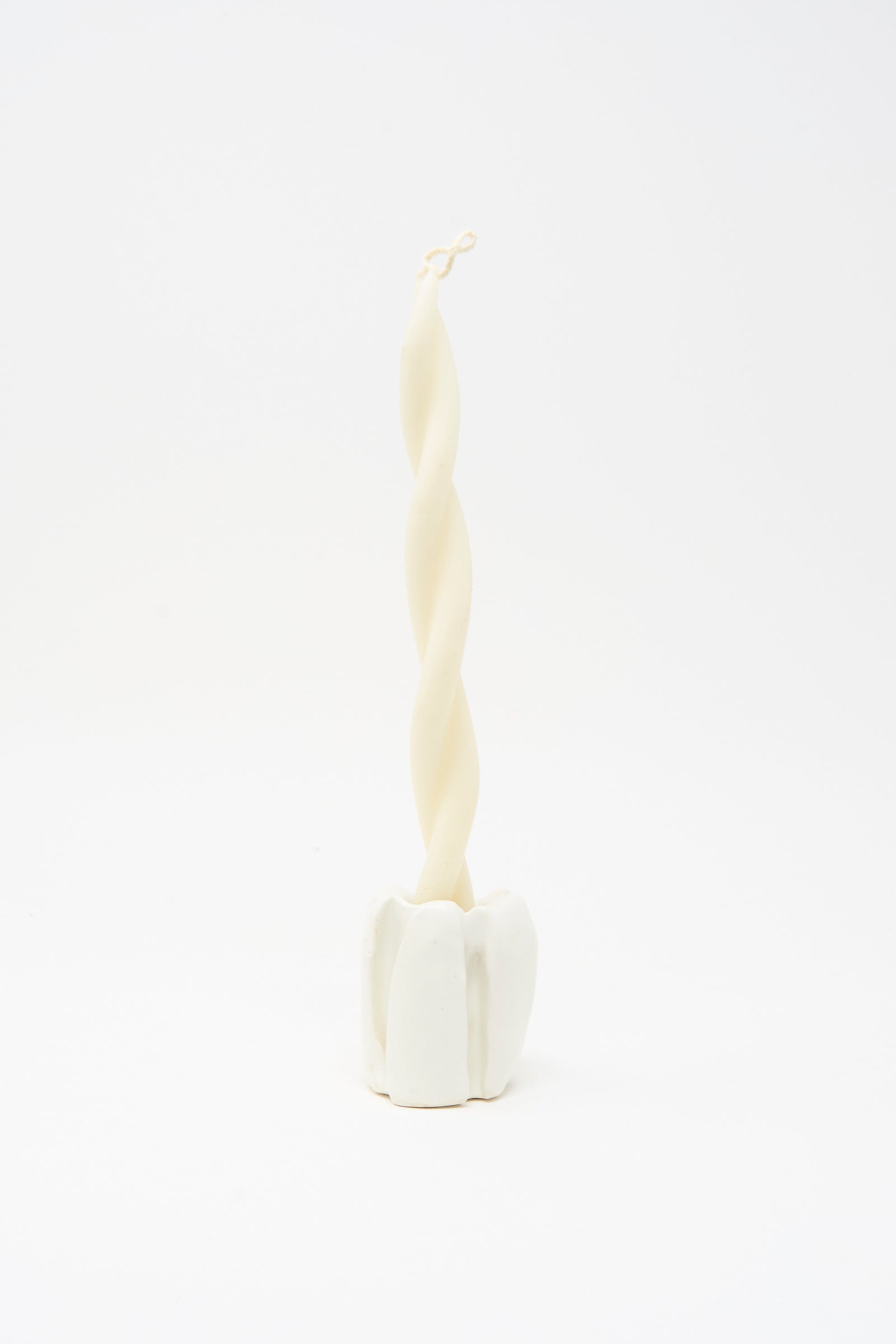A twisted white candle stands upright in the MONDAYS Ribbed Candleholder in White, handmade in Brooklyn, set against a plain white background.