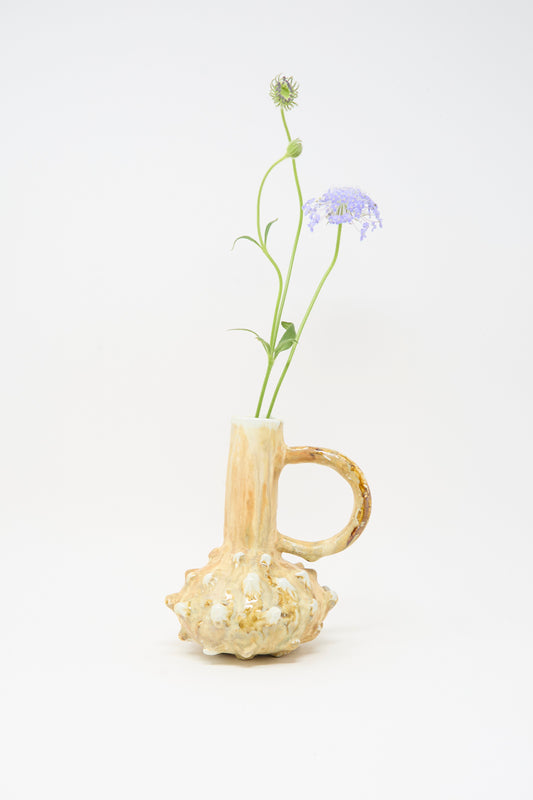 The MONDAYS Soda-Fired Bottle Vase No. 7 features a textured, bulbous beige ceramic base and holds two long-stemmed purple flowers against a plain white background.