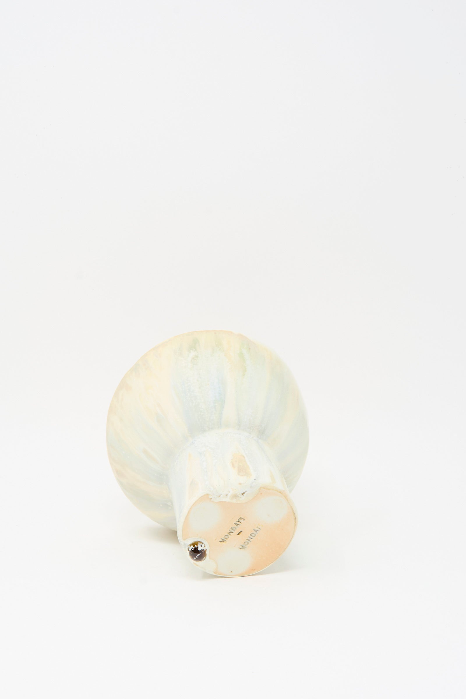 The MONDAYS Soda-Fired Pedestal Bowl, handmade in porcelain with a rounded top and flat base, lies on its side next to a small metallic ball on a white background.