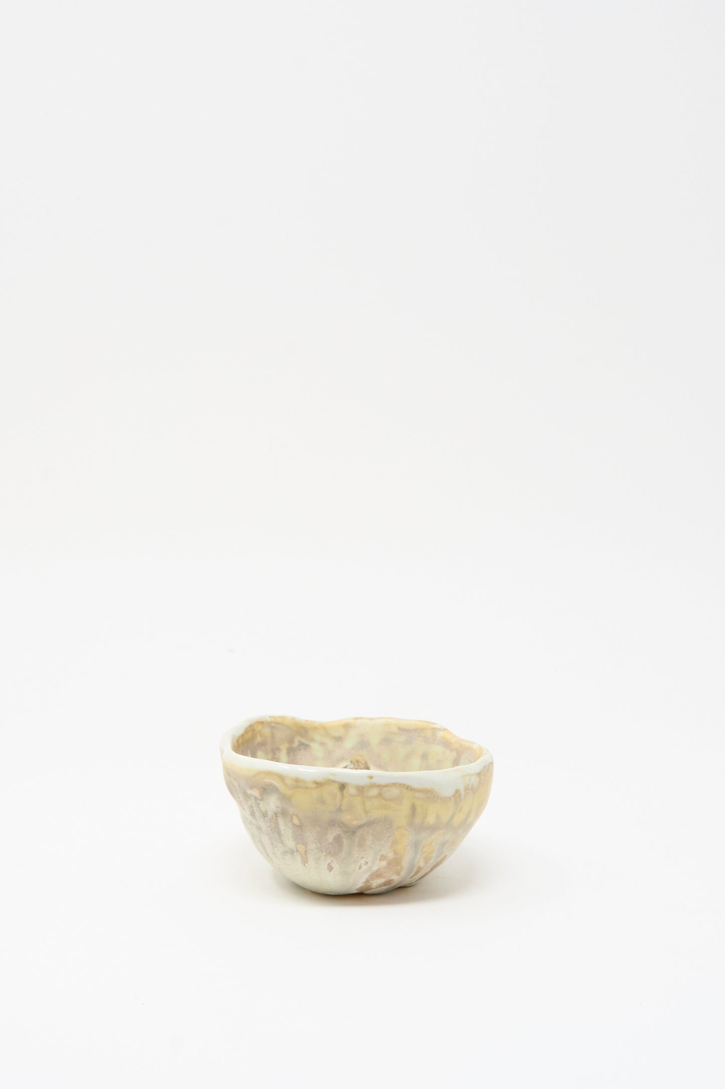 The MONDAYS Soda-Fired Pinched Bowl I, a small handmade bowl with an irregular pinched rim and a mottled light beige glaze, is displayed on a plain white background.