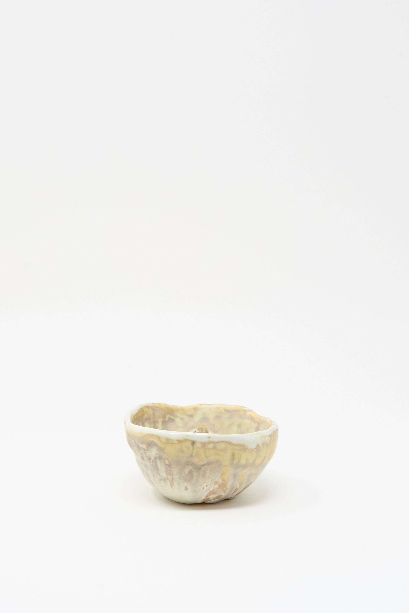 The MONDAYS Soda-Fired Pinched Bowl I, a small handmade bowl with an irregular pinched rim and a mottled light beige glaze, is displayed on a plain white background.
