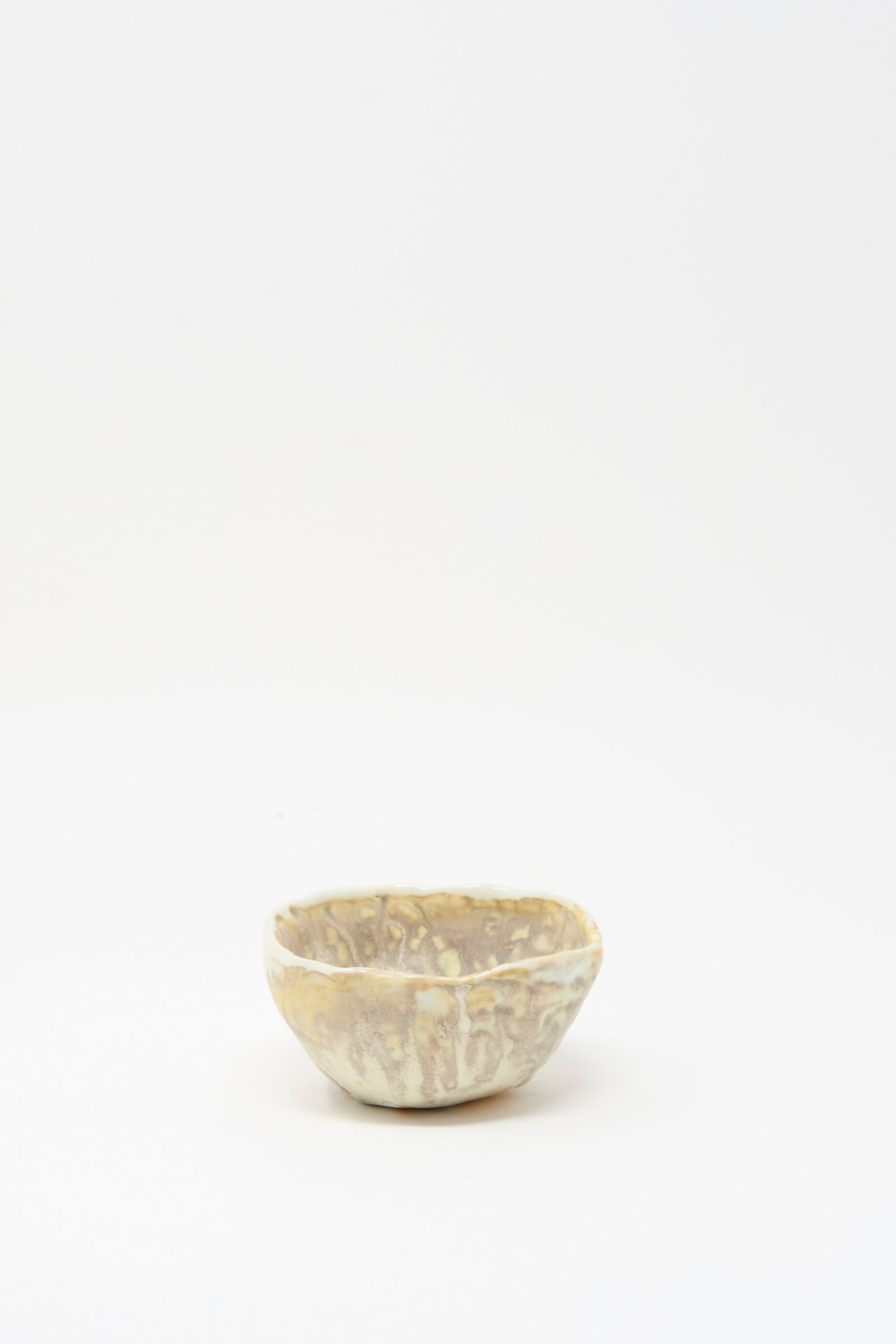 The Soda-Fired Pinched Bowl I by MONDAYS is a small, round handmade bowl featuring a textured light beige and brown surface, shown on a plain white background.